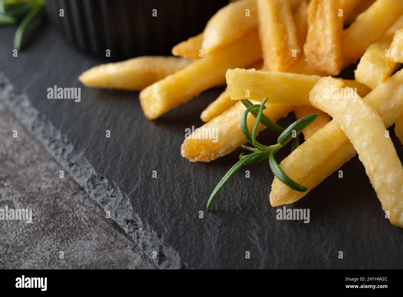 Hausgemachte Pommes Frites und Rosmarin auf einem schwarzen Schieferbrett Stockfoto
