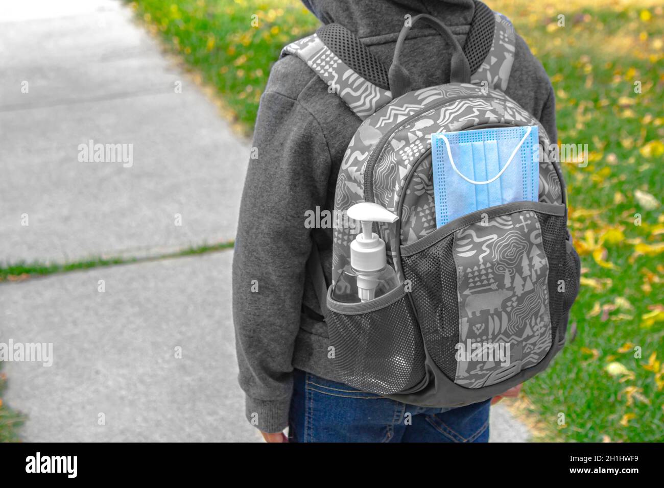 Ein Kind mit einer Schultasche mit Gesichtsmaske Und Händedesinfektionsmittel auf einer Tasche Stockfoto