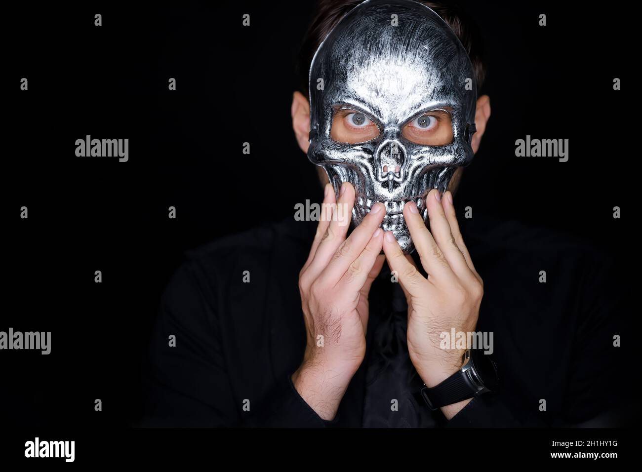 Ein Mann, der eine Skelettmaske trägt, korrigiert sie mit seinen Händen Stockfoto