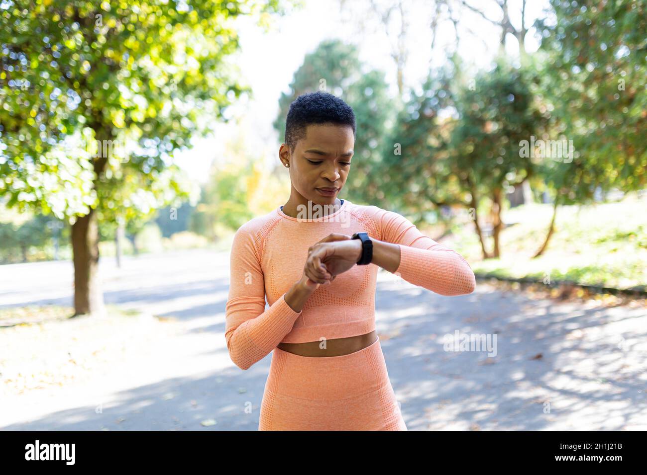 afroamerikanische Athletin wählt vor dem Training ein Fitnessprogramm auf einem Armband, im Herbstpark, einen gesunden aktiven Lebensstil Stockfoto