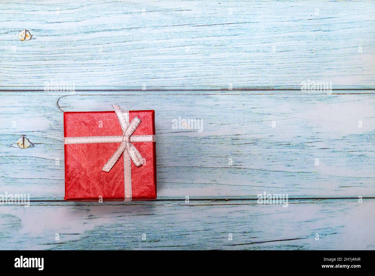Weihnachtskonzept. Weihnachtskarte mit einem roten Paket auf einem blauroten Tisch. Kopieren Sie den Platz auf der rechten Seite für Ihre Grußnachricht. Stockfoto