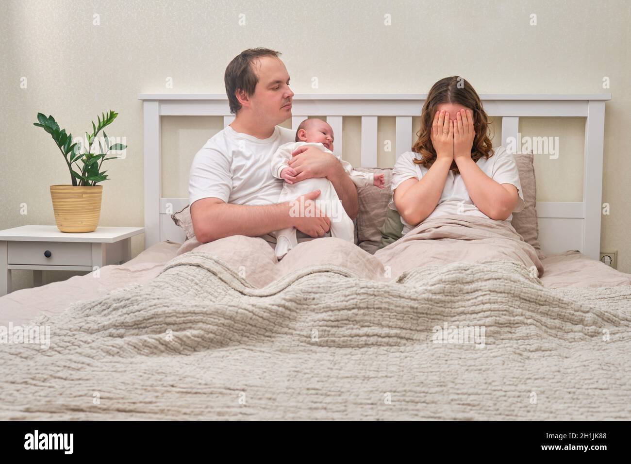 Ein Vater mit einem kleinen Jungen und einer Mutter, die bei postpartaler Depression weint, Eltern und ein Kleinkind auf einem Heimbett. Probleme eines Mannes und einer Frau mit einem Stockfoto