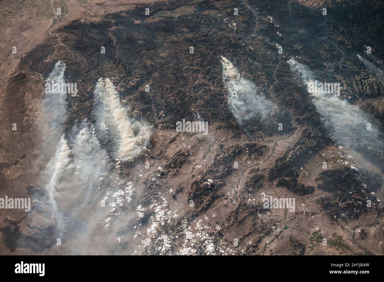 Die Erde von der Internationalen Raumstation aus gesehen: Idaho, USA. August 2013. Die dunklen Gebiete sind alle bewaldete Berge. In dieser bergigen Region sind mehrere Brände zu beobachten, die große Rauchwolken erzeugen, die meist durch Blitzschlag ausgelöst werden. Dieses Bild zeigt das übliche Muster von westlichen Winden, die Rauch in östlicher Richtung transportieren. Eine optimierte und verbesserte Version eines NASA-Bildes / Credit NASA. Stockfoto