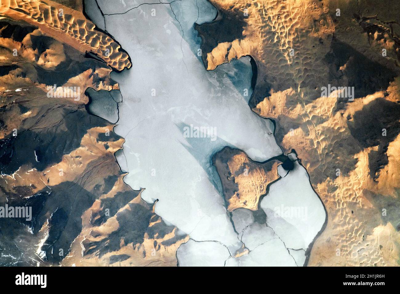Landsat-Bilder der Erde: Schatten akzentuieren die Topographie in und um den Ulaagchinii Khar Nuur (See) in der Mongolei auf diesem Sonnenaufgangsfoto von der Internationalen Raumstation ISS. Beachten Sie die großen und kleinen Avgash-Inseln. Risse durchdringen die eisbedeckte Oberfläche des Sees, und Dünen umsäumen das Ufer. Die kalte, flache Eisoberfläche steht im Kontrast zu den markanten, rollenden Wellen von Sanddünen. Eine optimierte und digital verbesserte Version eines NASA-Bildes/Credit NASA Stockfoto