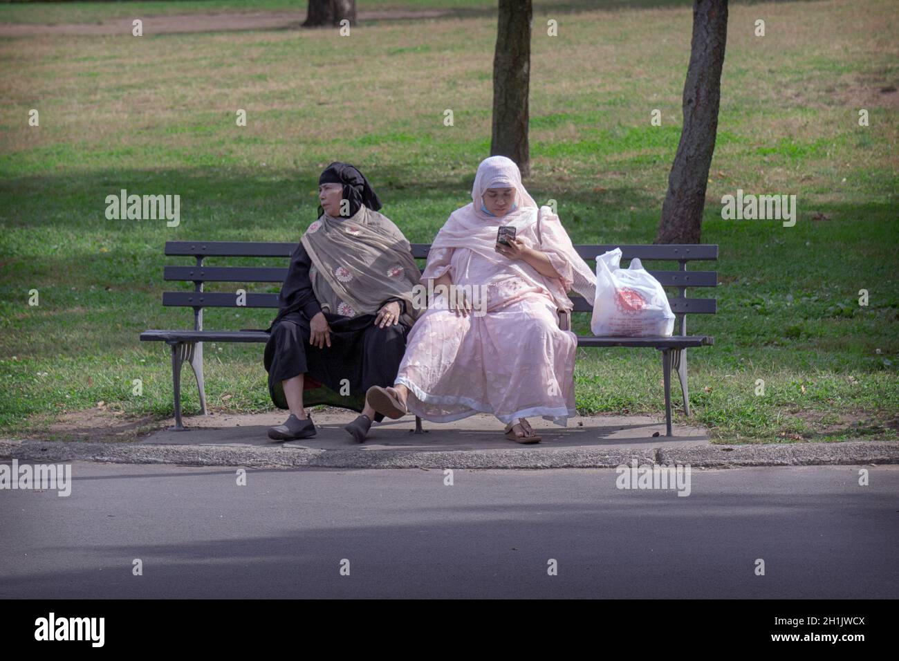 2 muslimische Frauen in traditioneller Kleidung teilen sich eine Bank im Lllushing Meadows Corona Park, Queens, New Ork City. Stockfoto