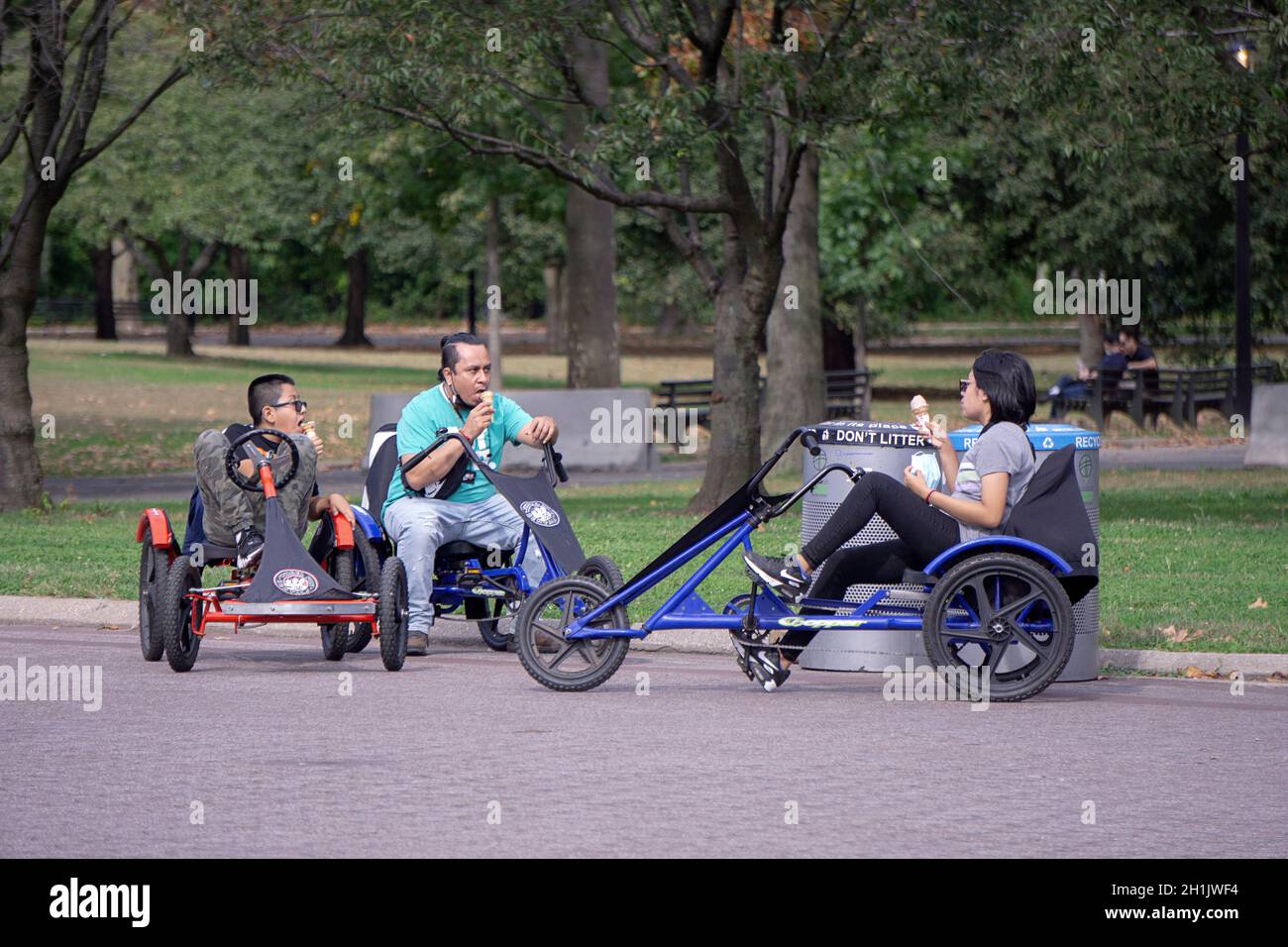 Eine Familie auf dem Rad Spaß Dreiräder halten für eine Eiscreme Pause. Im Flushing Meadows Corona Park in Queens, New York City. Stockfoto