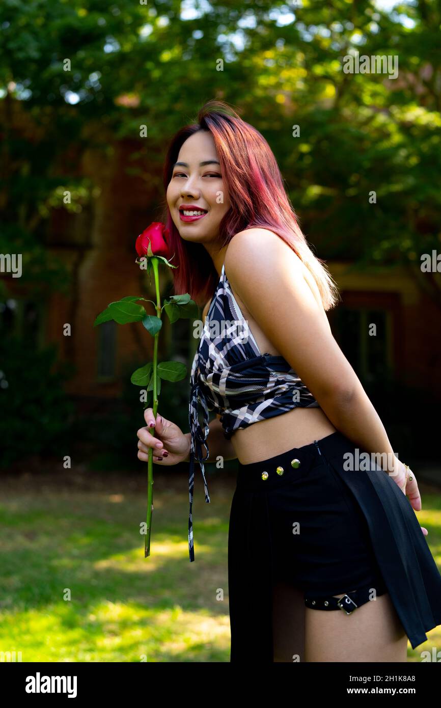 Junge asiatische Frau hält eine Rose in einem Garten Einstellung Stockfoto