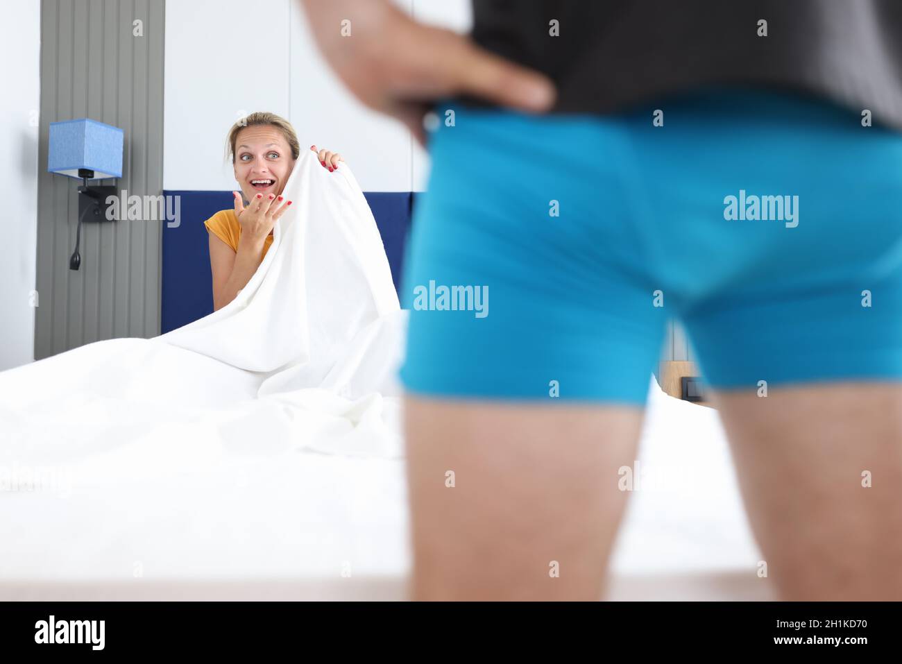 Frau, die auf dem Bett sitzt, sieht den Mann in kurzen Hosen aus der Nähe an Stockfoto