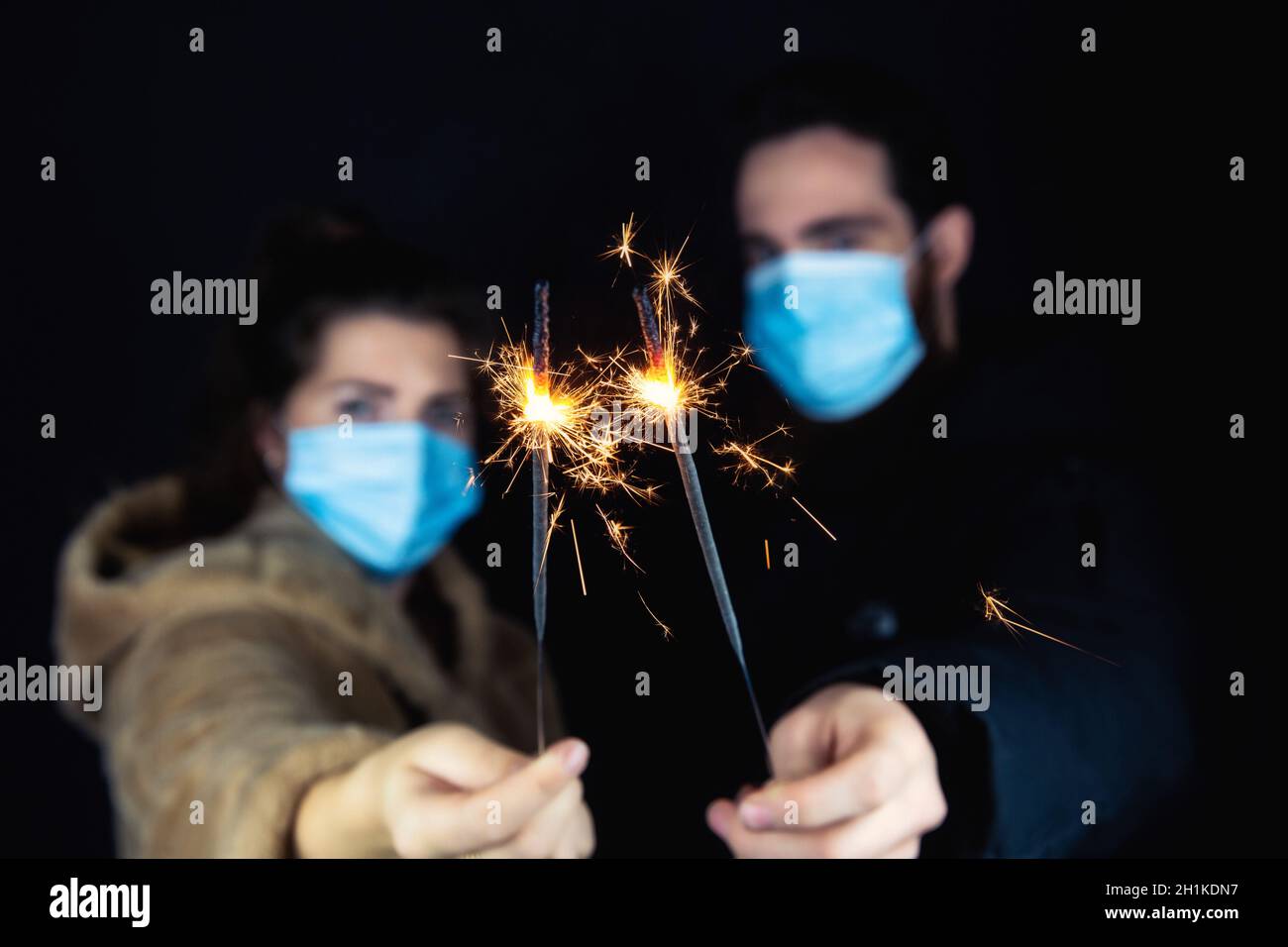 Junges Paar mit schützenden Gesichtsmasken für Coronavirus und mit Wunderkerzen für Silvester, 2021 und Covid-19 Konzept Stockfoto