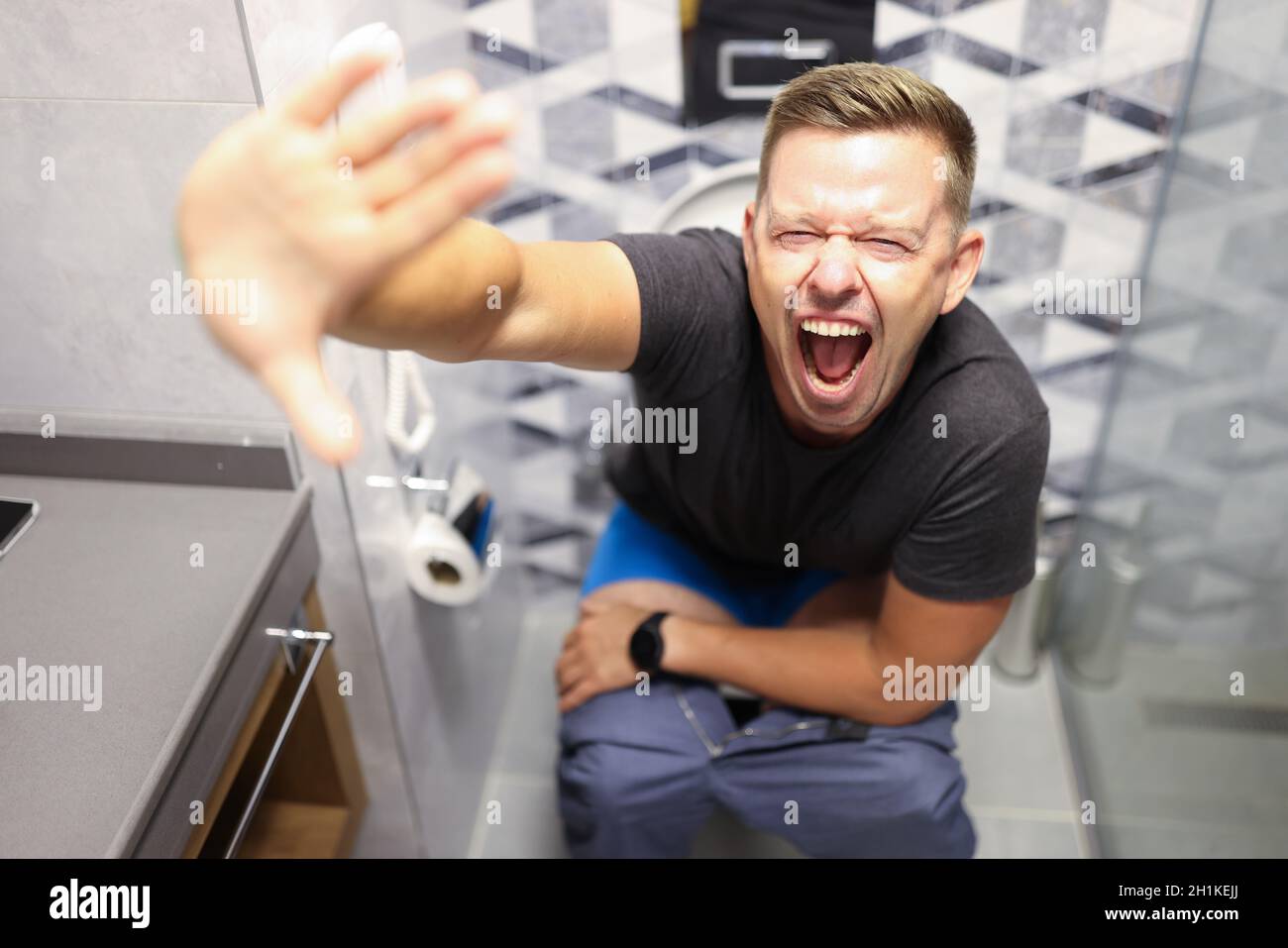 Ein junger Mann schreit, während er in der Nähe auf der Toilette sitzt Stockfoto