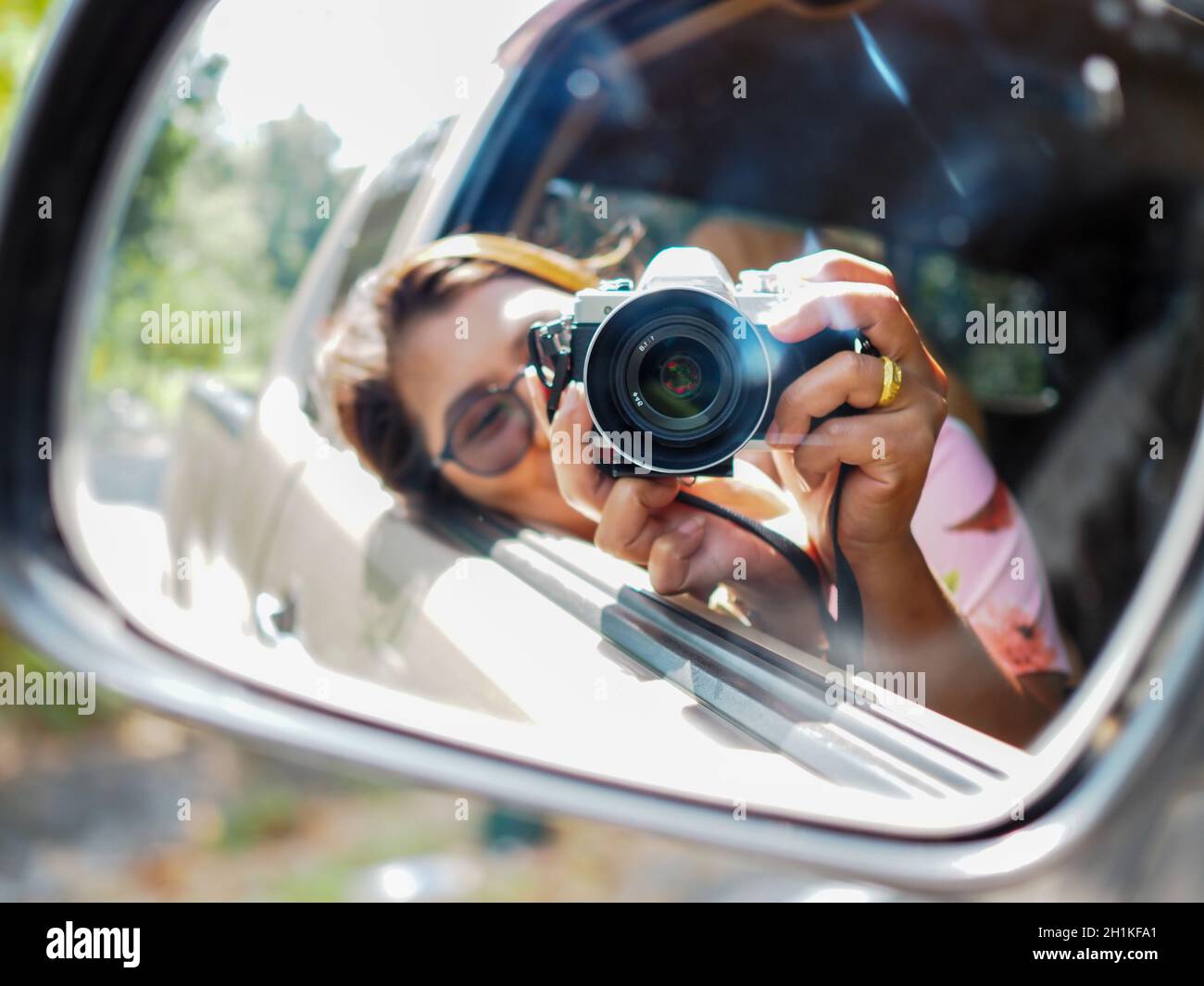 Eine junge Frau hielt eine Digitalkamera und machte ein Bild von sich selbst lächelnd im Autospiegel reflektiert. Fokus auf Kamera. Stockfoto