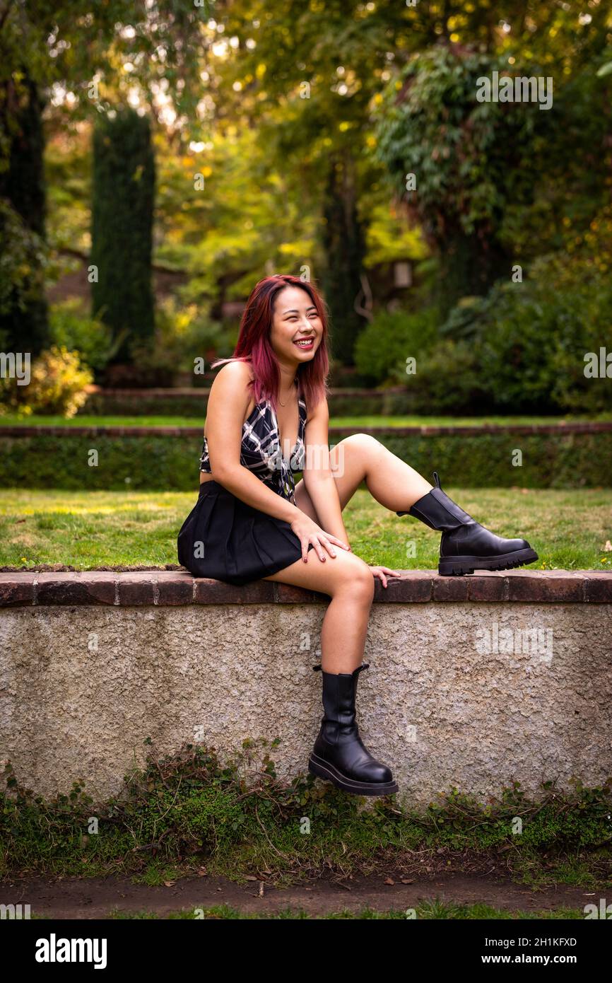 Junge asiatische Frau sitzt auf einer Gartenwand Stockfoto