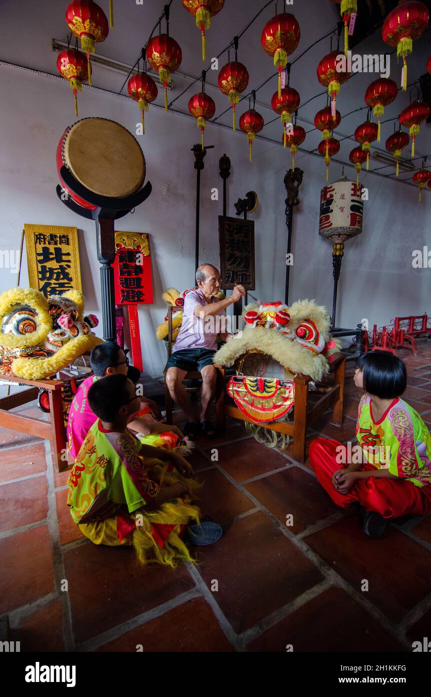 Georgetown, Penang/Malaysia - Jul 08 2016: Ein alter Mann putzt den chinesischen Löwentanzkopf mit Pinsel und Jugendliche sitzen auf dem Boden. Stockfoto