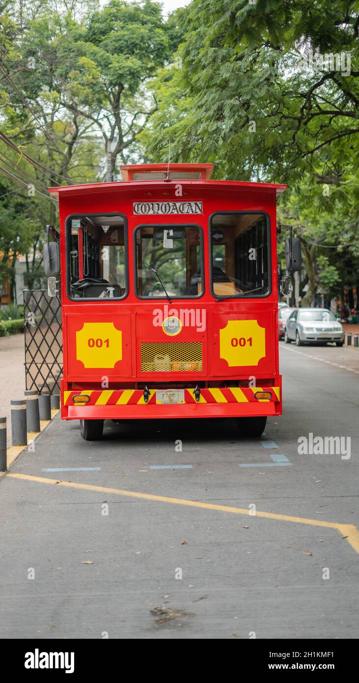 Portraitbild einer roten und gelben Straßenbahn, die unter den Bäumen von Coyoacan fährt Stockfoto