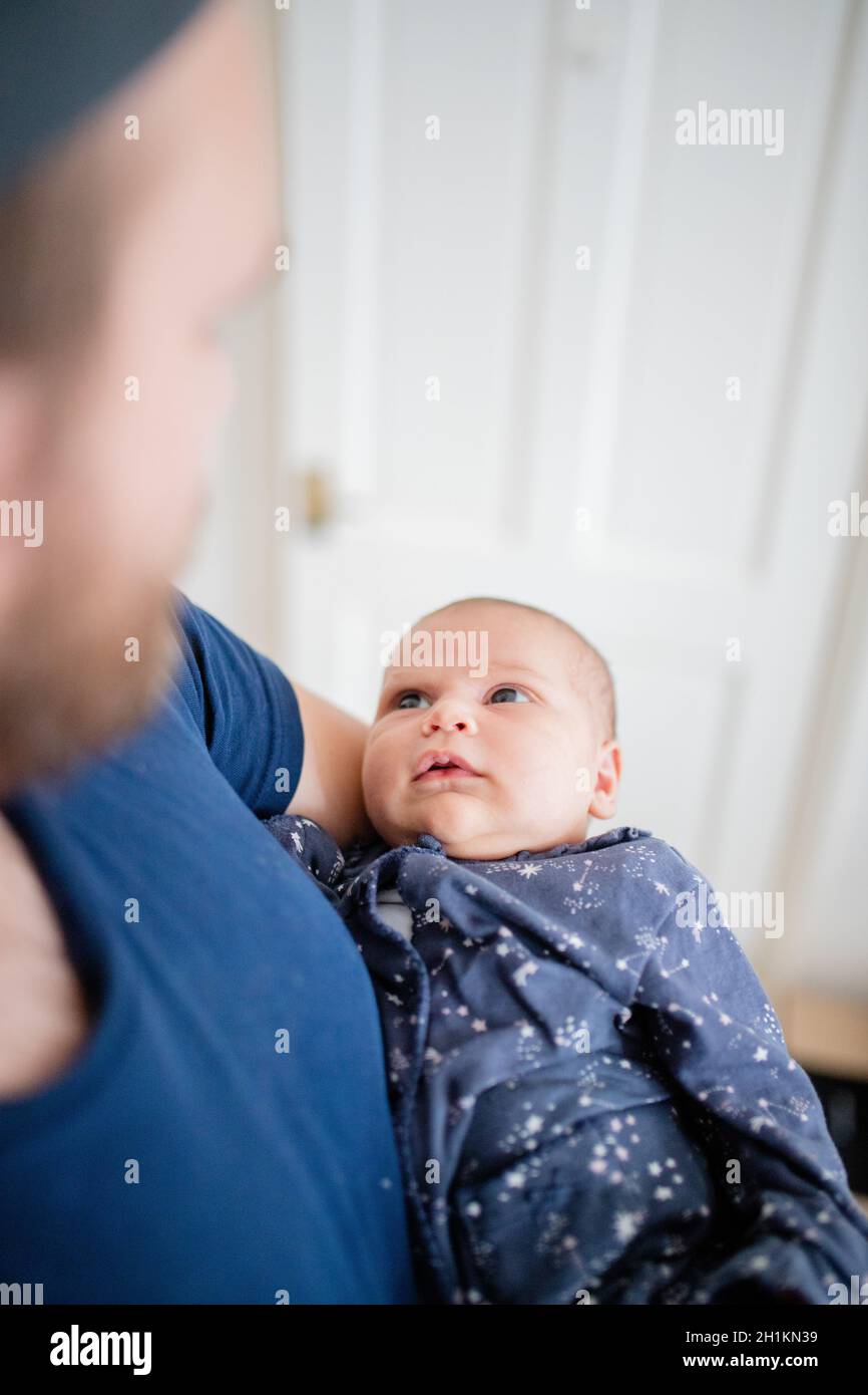 Portrait-Stil Bild eines Babys in den Armen ihres Vaters mit einer verschwommenen weißen Tür als Hintergrund gehalten Stockfoto