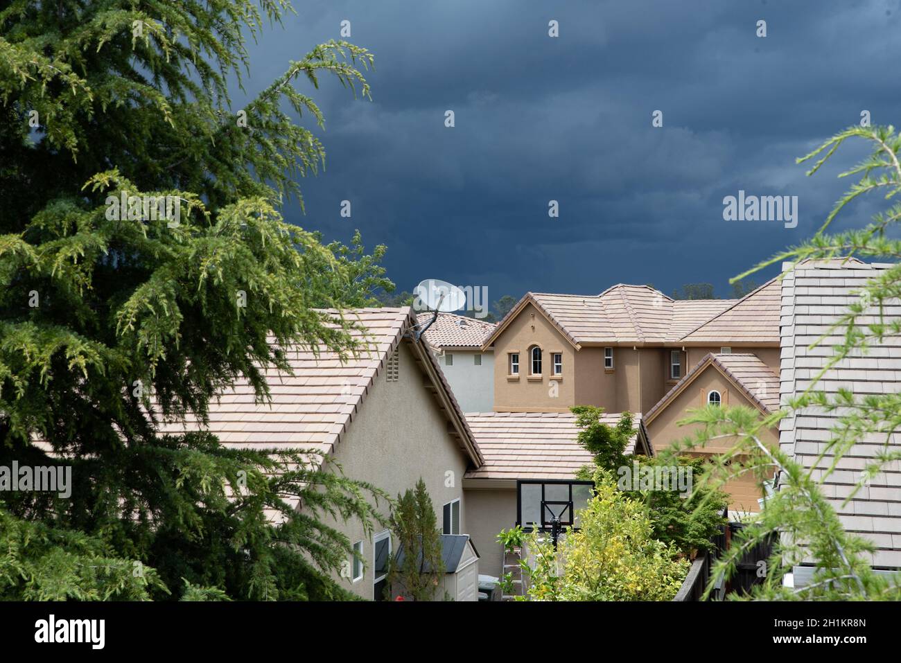 Auf dem Dach eines Vorstadthauses mit riesigen Sturmwolken am Himmel erscheint eine Einzelschüssel-Satellitenschüssel. Stockfoto