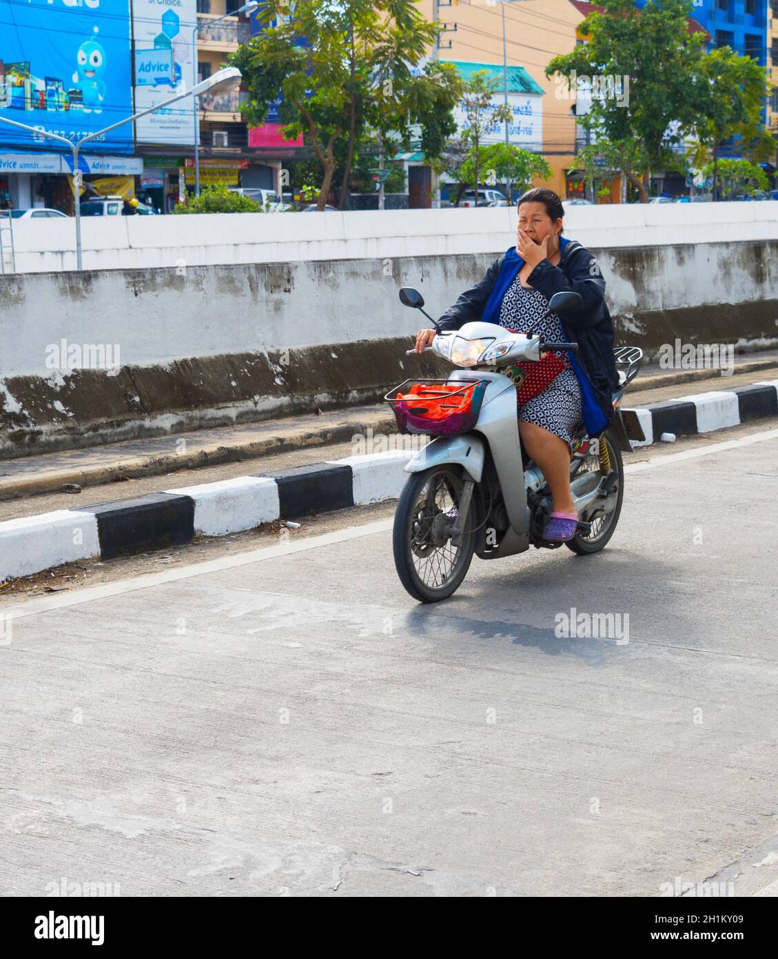 CHIANG MAI, THAILAND - 12. JANUAR 2017: Frau gähnt, als sie im Straßenverkehr ein Motorrad fährt. Stockfoto