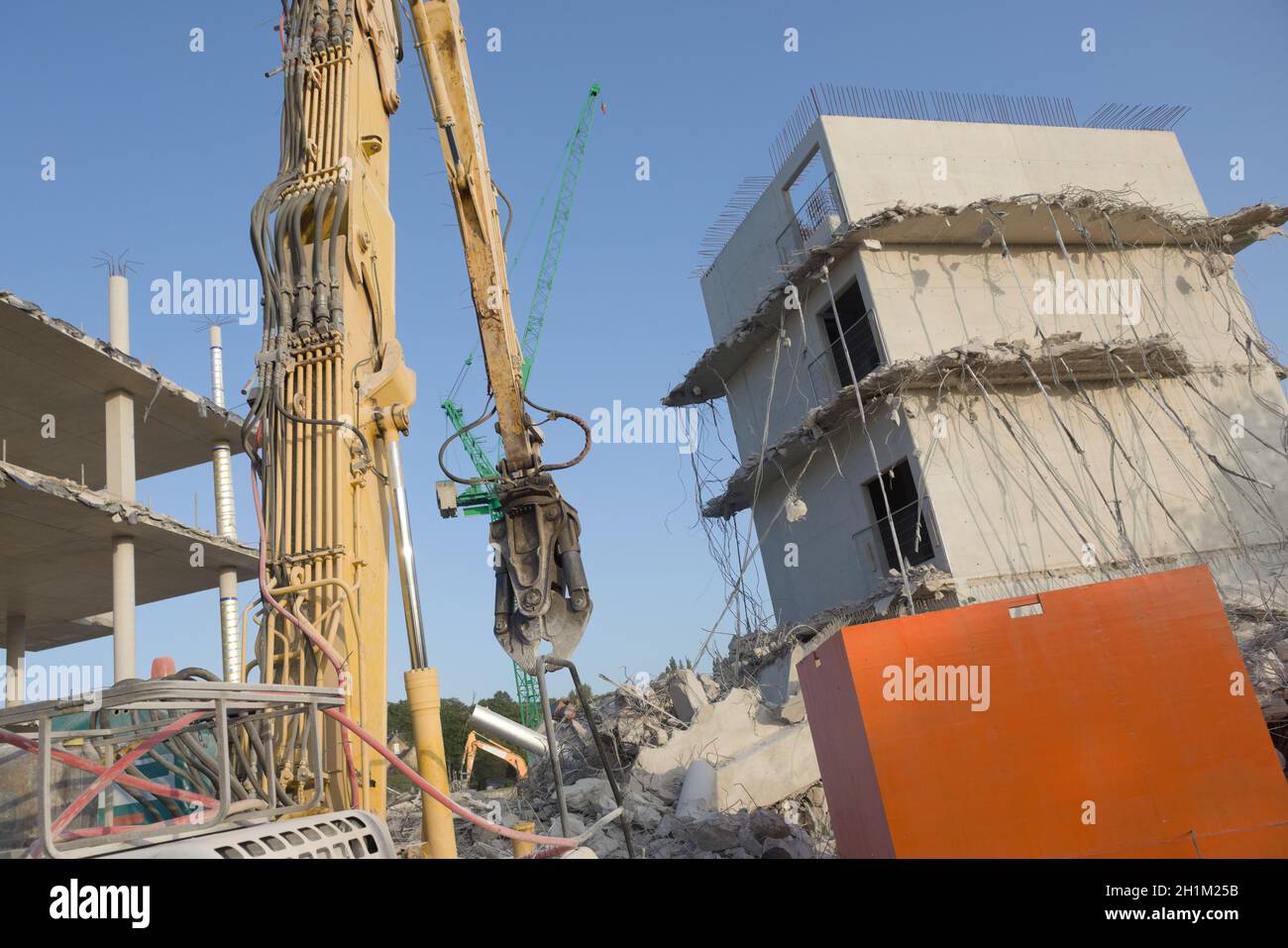 Betonschutt und hängende Stahlseile auf dieser Abrissstelle, großer, hoch reichender Abrissbagger im Vordergrund, mit Turmkran dahinter Stockfoto