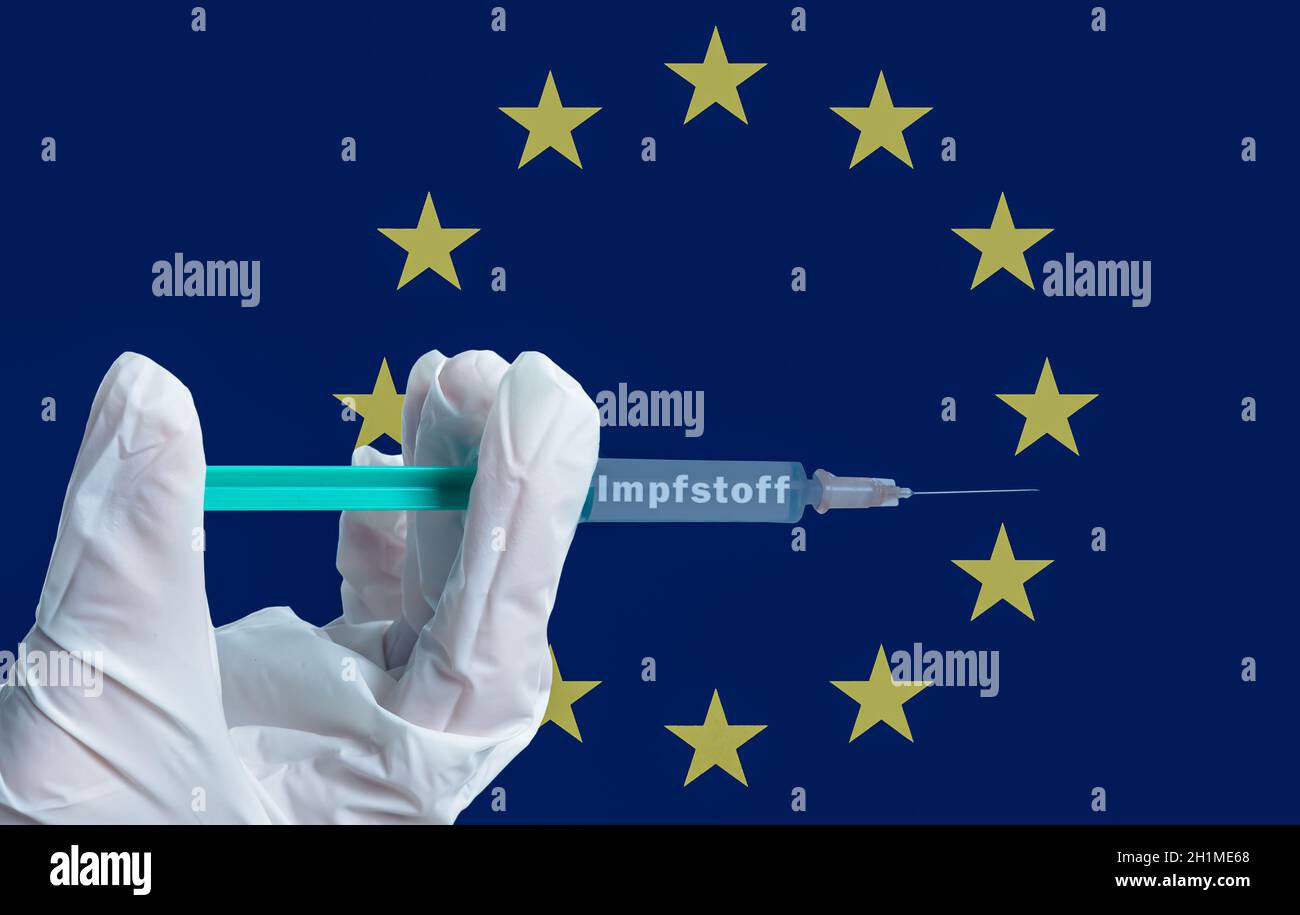 Eine Hand hält eine Spritze mit der deutschen Aufschrift Impfstoff Symbolisch vor einer europäischen Flagge Stockfoto