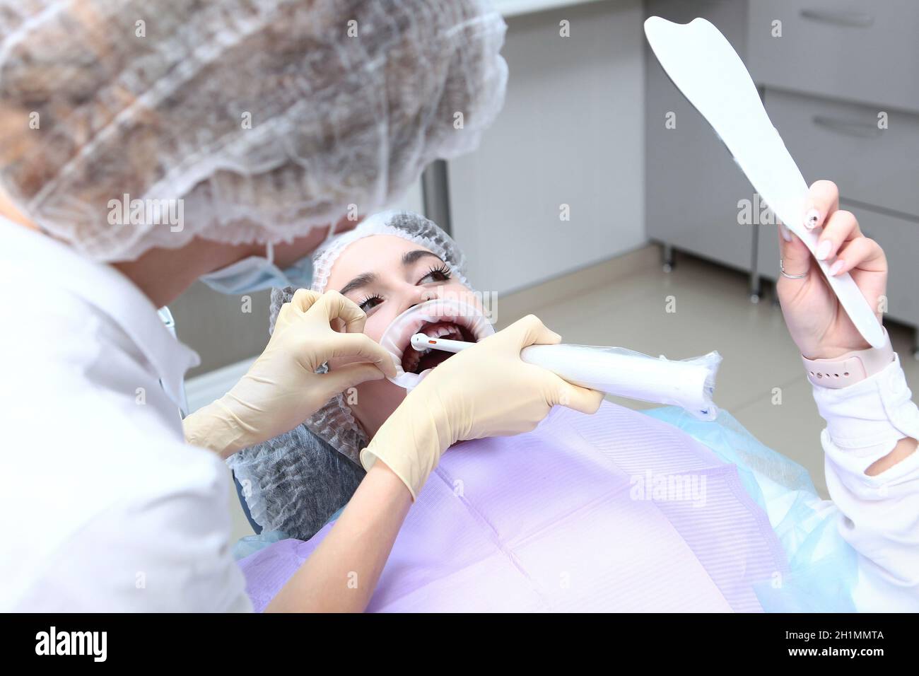 Professionelle Zahnreinigung.Elektrische Zahnbürste in den Händen eines  Zahnarztes. Ein junges Mädchen bei einem Zahnarzttermin schaut sich selbst  im Spiegel an.Traini Stockfotografie - Alamy