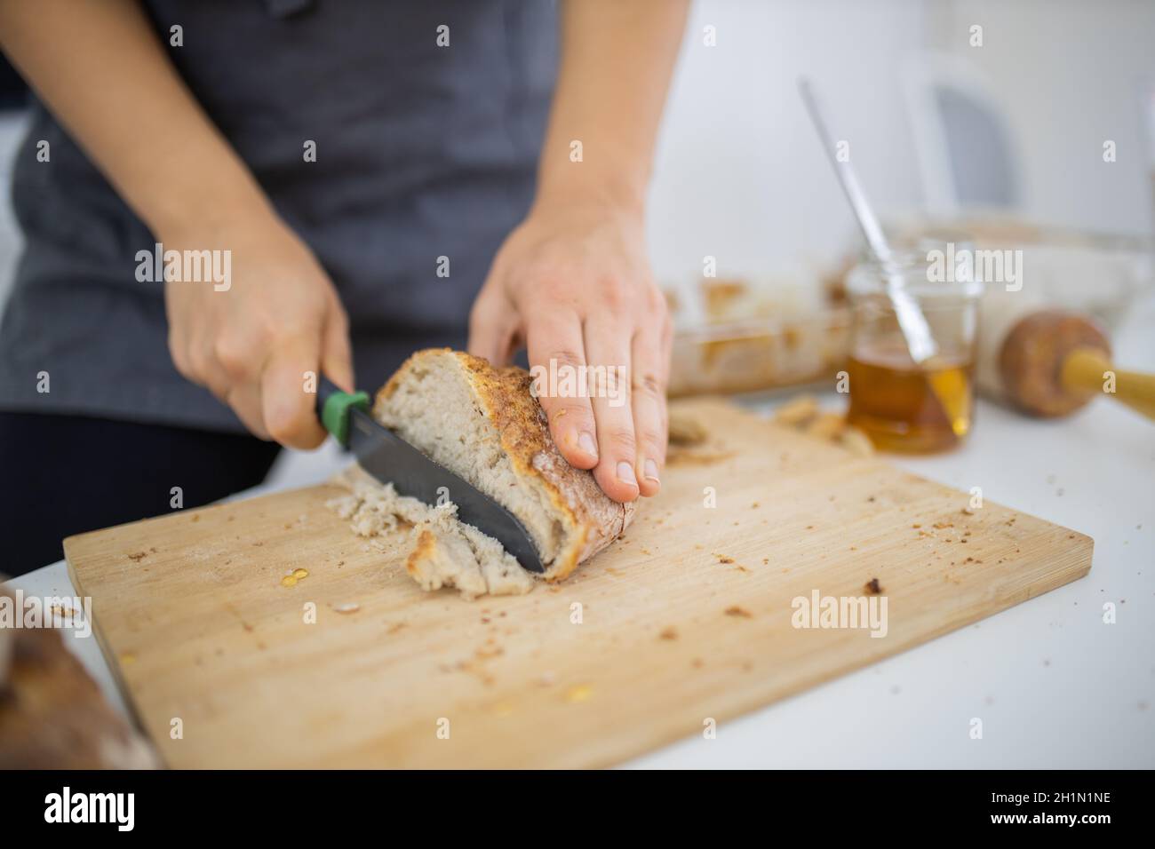 Weibliche Hände schneiden Brot auf Holz Schneidebrett. Frau sorgfältig schneiden Sauerteig Brot über weißem Tisch. Gesunde Zubereitung von Mahlzeiten Stockfoto