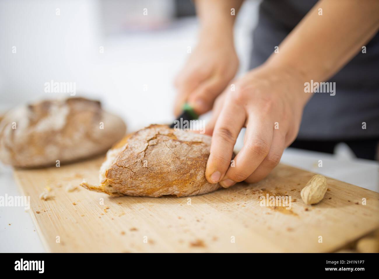 Weibliche Hände schneiden Brot auf Holz Schneidebrett. Frau sorgfältig schneiden Sauerteig Brot über weißem Tisch. Gesunde Zubereitung von Mahlzeiten Stockfoto