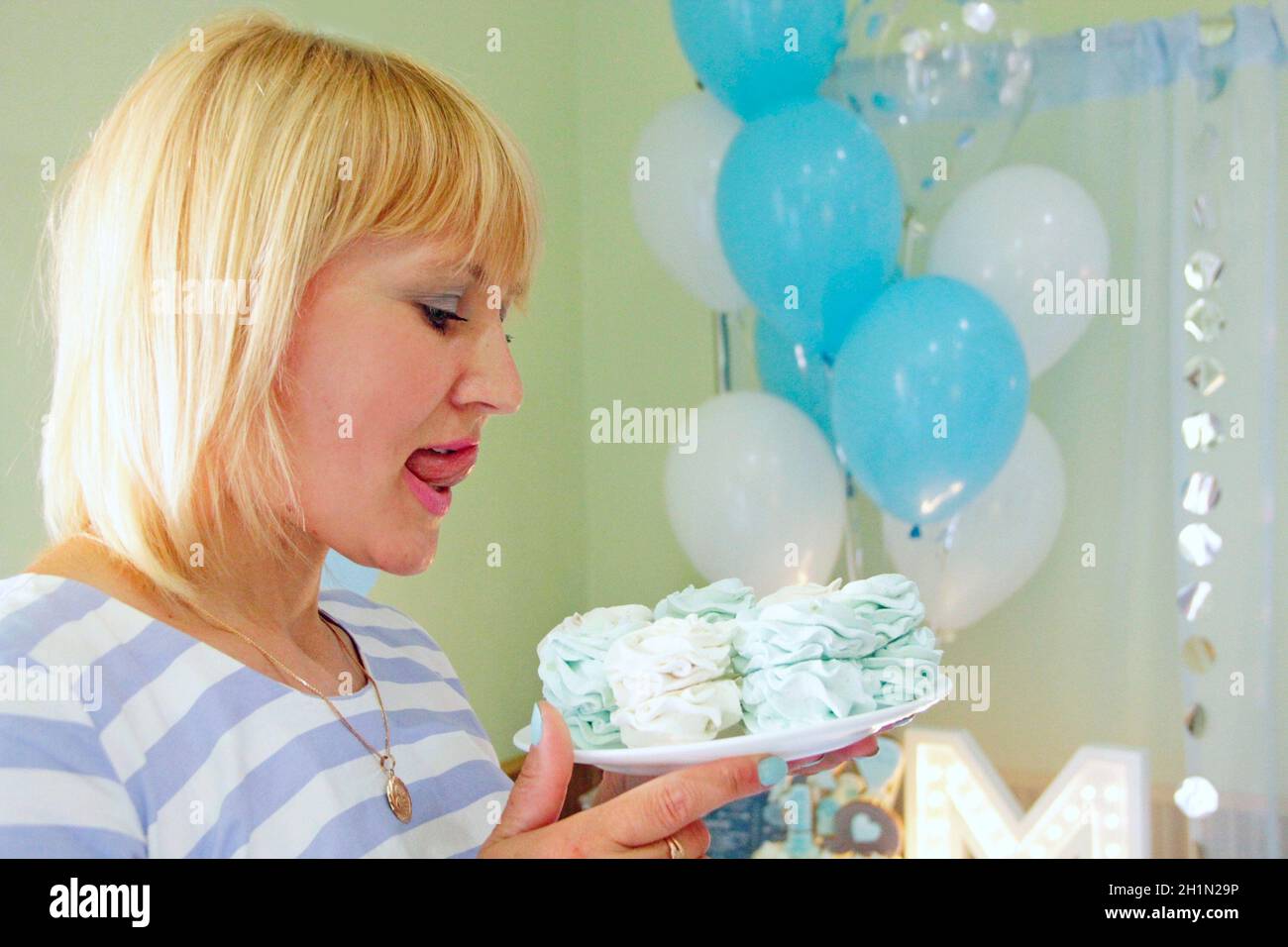 Schöne Frau beißende Zunge Blick auf Urlaub Kuchen. Eine aufrühme Frau, die einen leckeren Kekskuchen ansieht. Hübsche Frau, die festliche Meringue isst Stockfoto