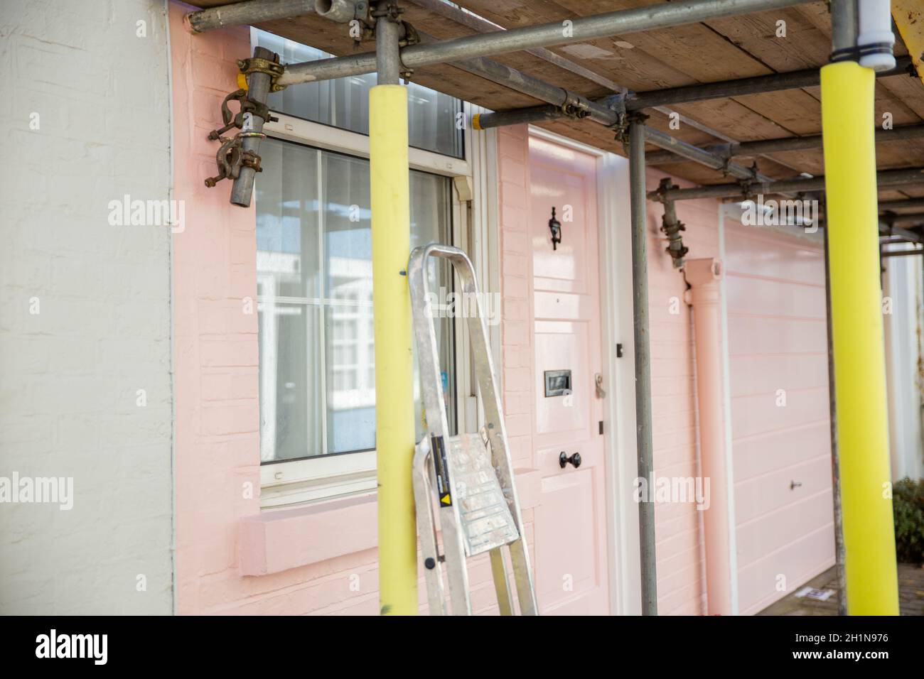 Ein gerüsttes Außenfenster und eine Tür eines pastellrosa britischen Hauses. Schönes buntes englisches Haus hinter Metallstruktur. Farbenfrohes Londoner Viertel Stockfoto