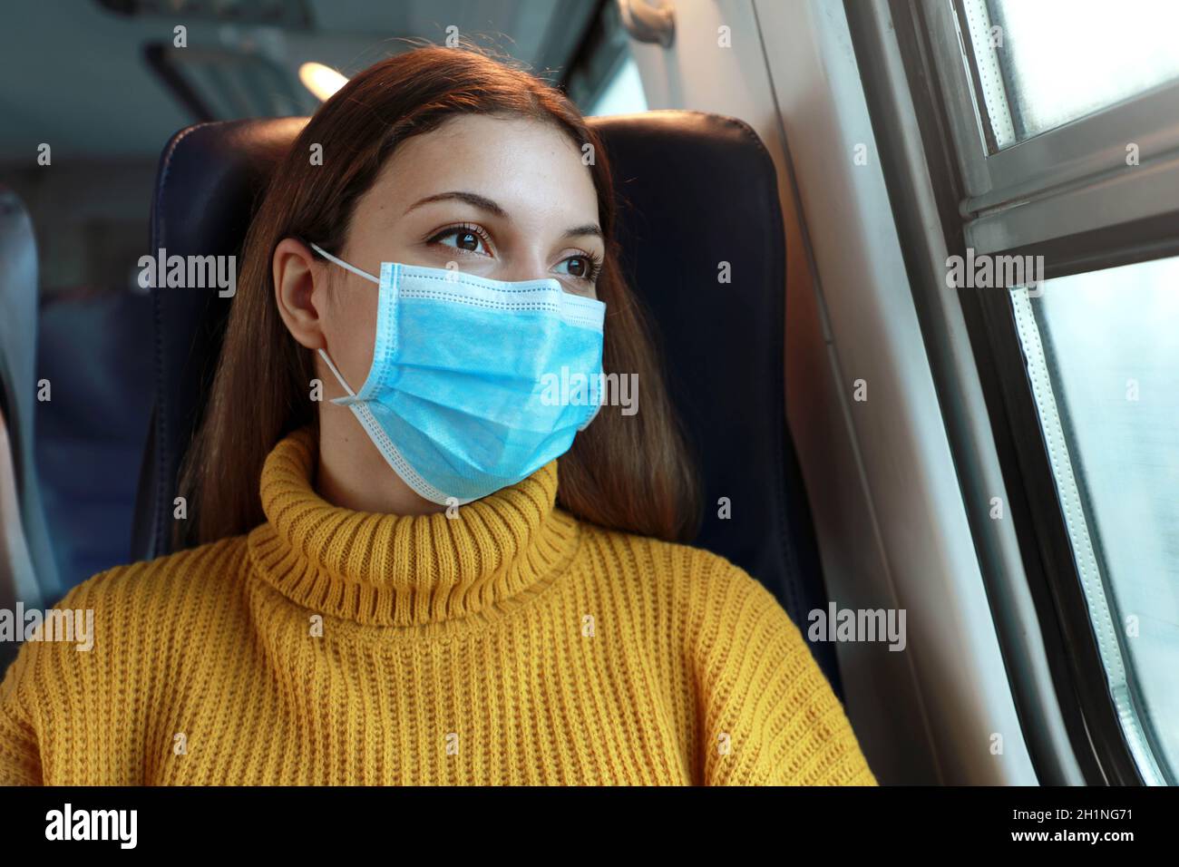 Nahaufnahme der weiblichen Pendler mit chirurgischen Gesichtsmaske Blick durch Zug Fenster. Zug Passagier mit Schutzmaske Reisen sitzen in Business cla Stockfoto