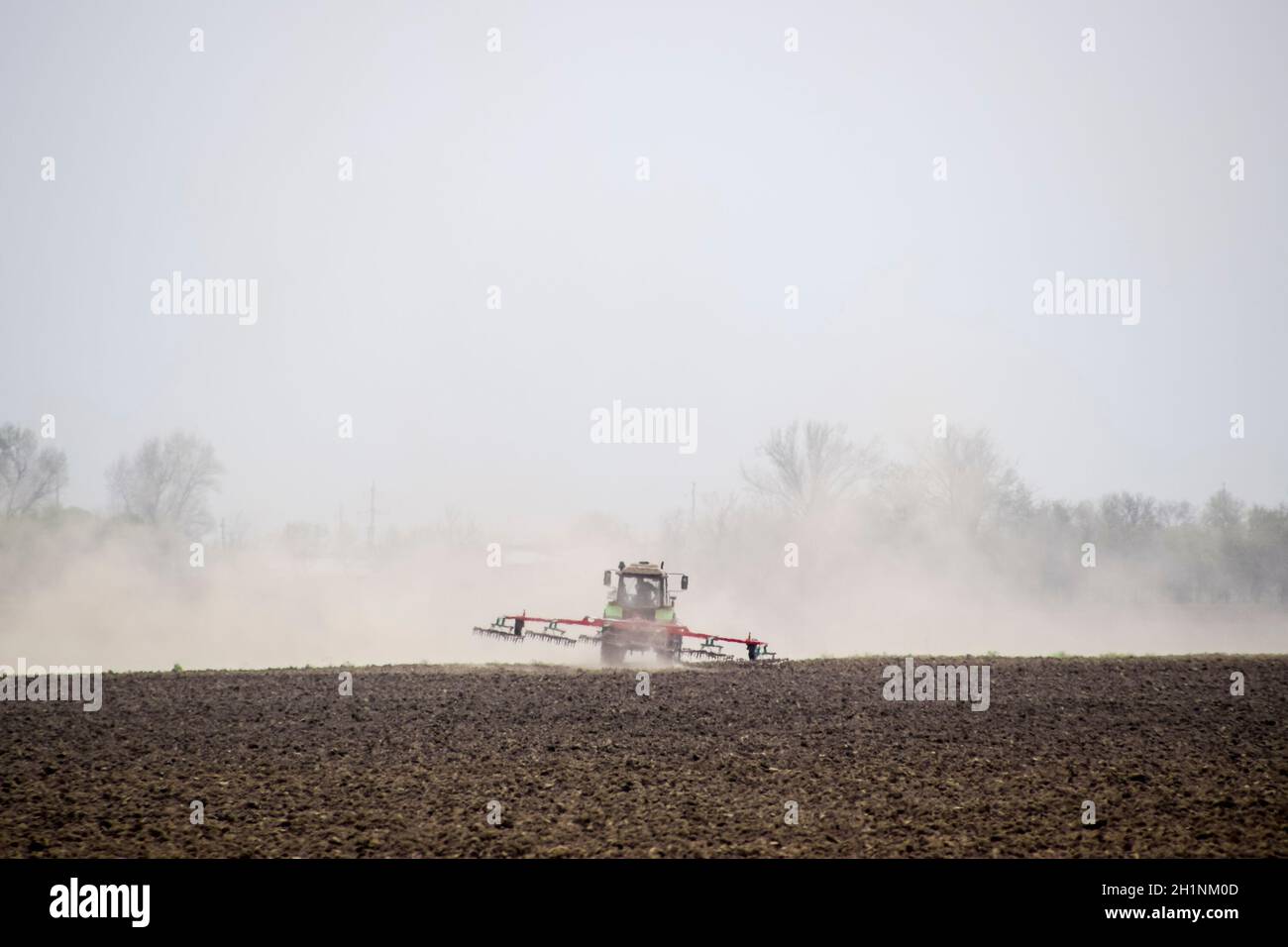 Der Traktor Eggen der Boden, auf dem Feld und schafft eine Staubwolke hinter sich. Stockfoto