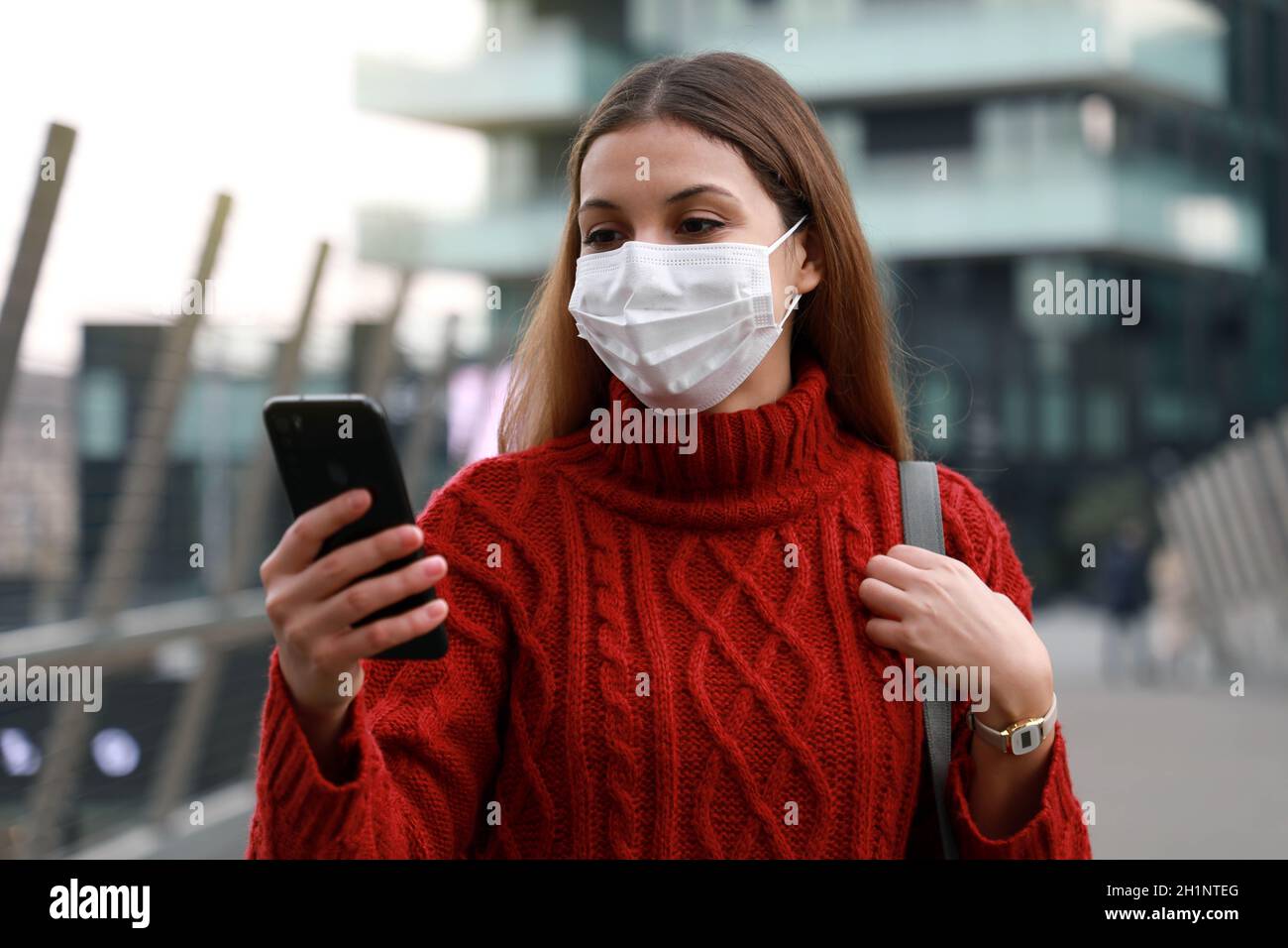 Portrait der Geschäftsfrau mit Schutzmaske zu Fuß in modernen Stadthintergrund mit Smartphone Stockfoto