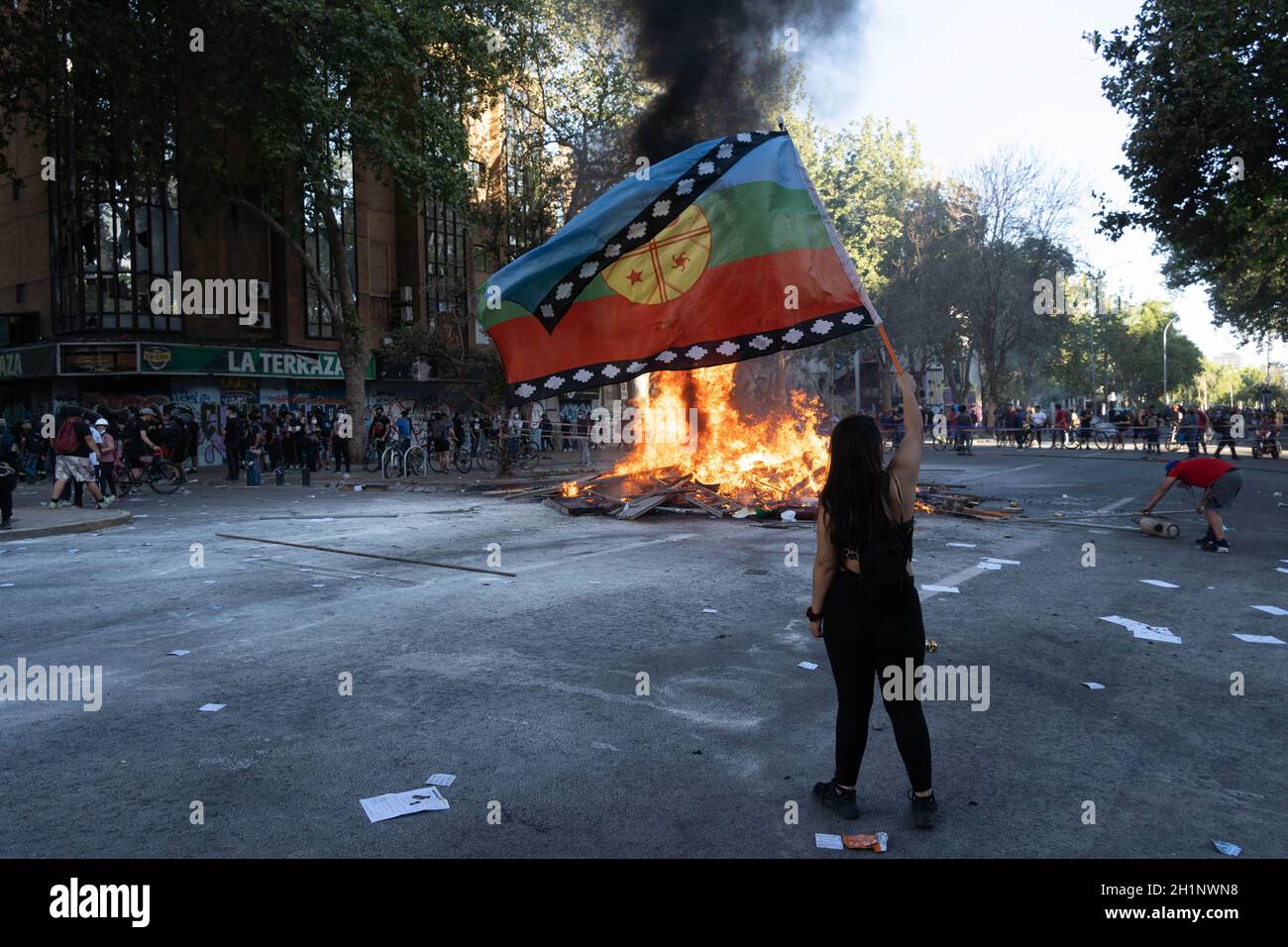 Santiago, Chile. Oktober 2021. Eine Frau fliegt während eines Protestes zum zweiten Jahrestag des sozialen Ausbruchs gegen die Regierung Sebastian Pinera mit einer Mapuche-Fahne vor einer Barrikade. (Bild: © Matias Basualdo/ZUMA Press Wire) Stockfoto