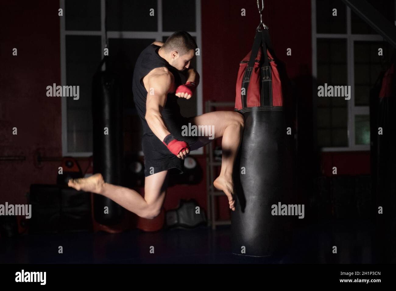 Kickboxen-Kämpfer mit Jumping Air-Kicks mit Knie auf Punch Bag. Kaukasischer Mann übt Kampfkunstausbildung im Urban Gym. Qualitativ hochwertige Phot Stockfoto