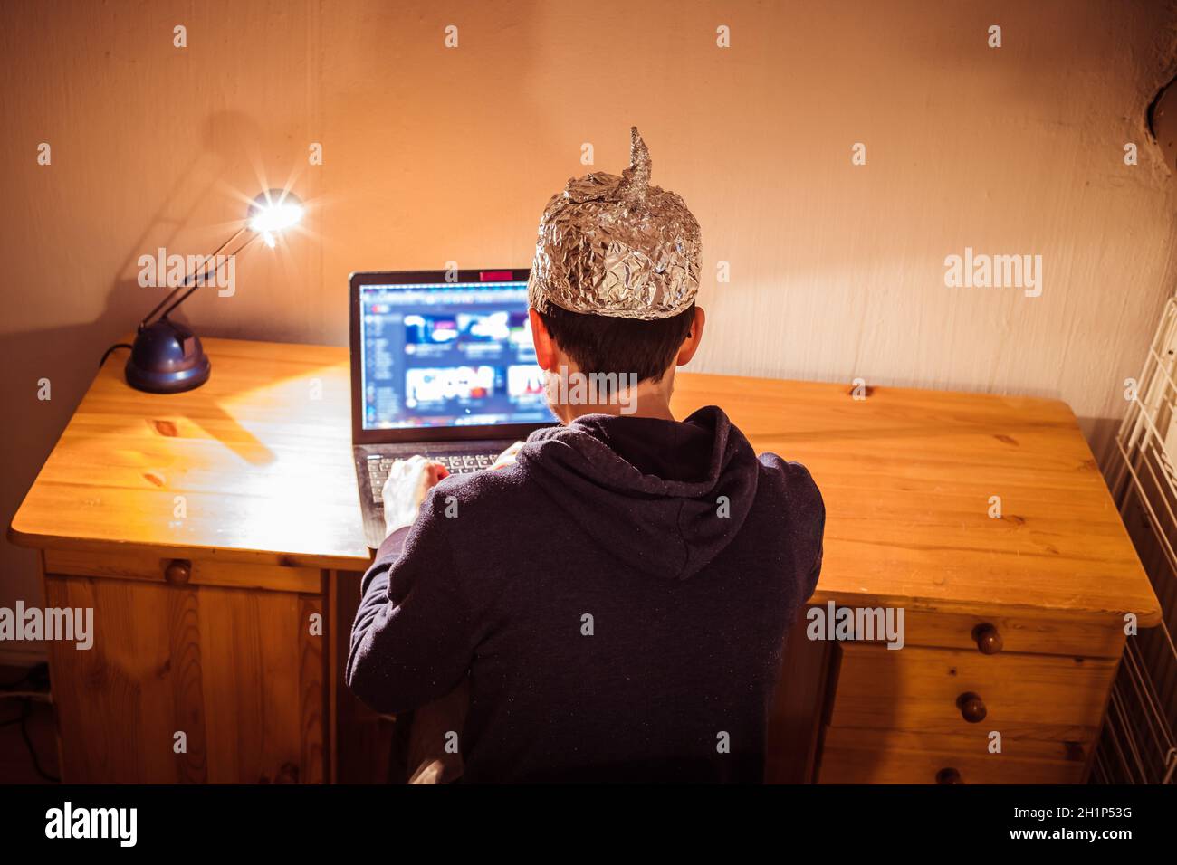 Der junge Mann mit Aluminiumkappe sitzt im dunklen Keller vor einem Laptop. Verschwörungstheorie Konzept Stockfoto