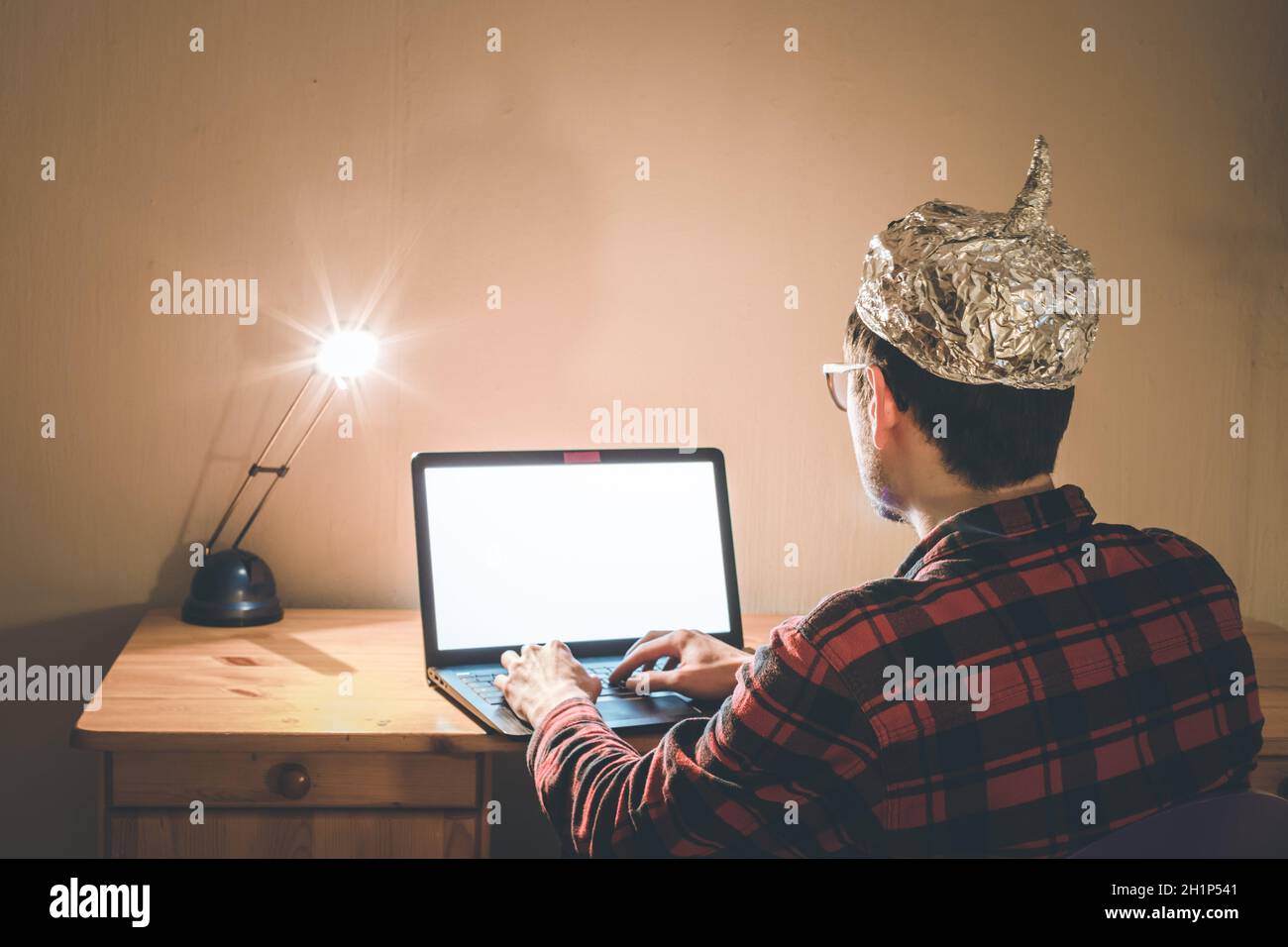 Der junge Mann mit Aluminiumkappe sitzt im dunklen Keller vor einem Laptop. Verschwörungstheorie Konzept Stockfoto