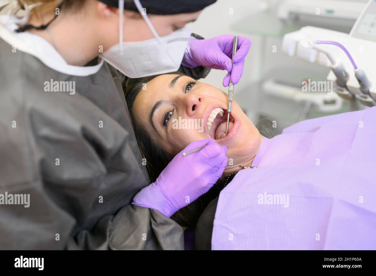 Junge weibliche Patientin besucht Zahnarztpraxis.schöne Frau sitzt am Zahnstuhl mit offenem Mund während der oralen Untersuchung, während der Arzt an den Zähnen arbeitet Stockfoto