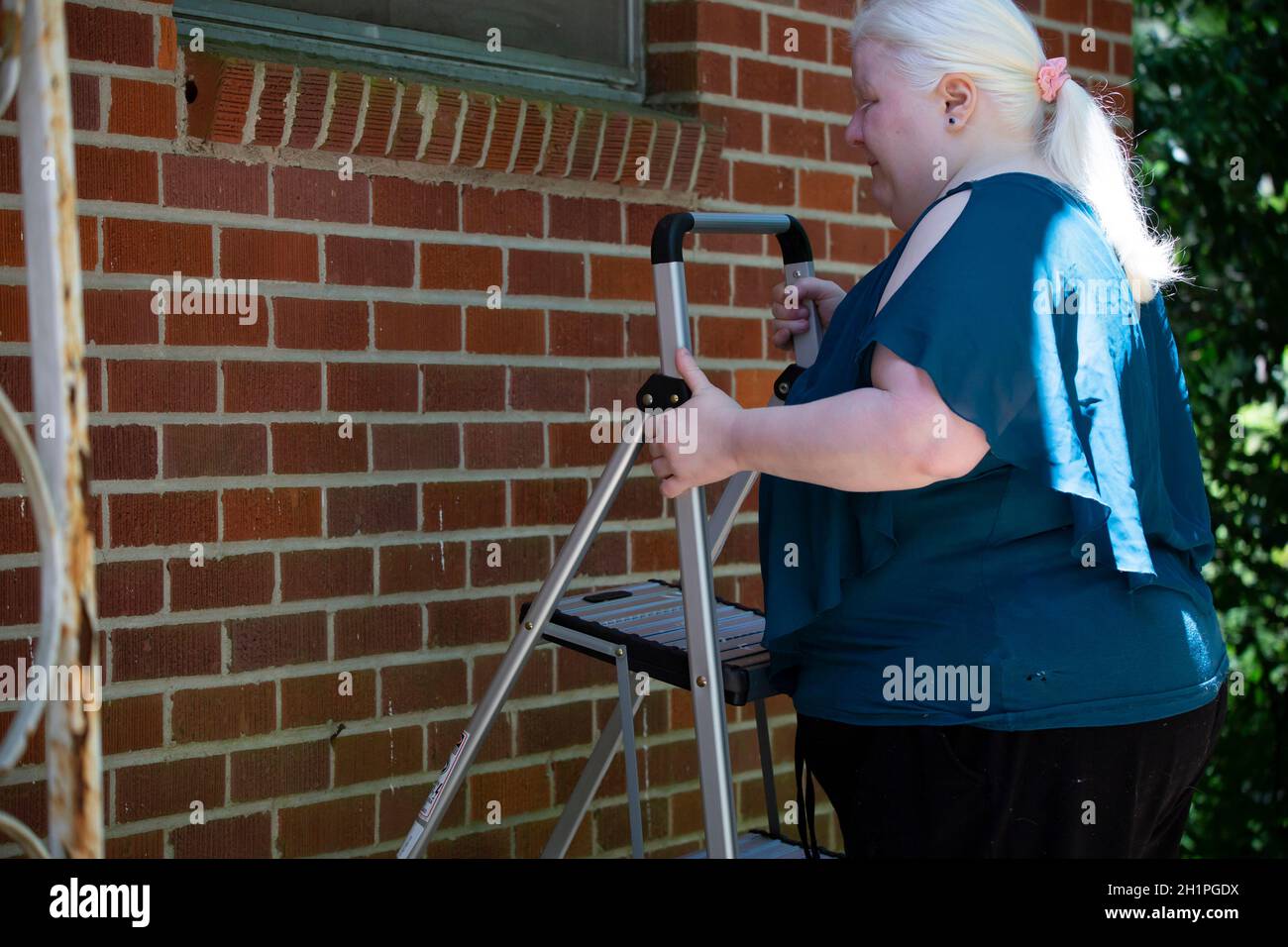 Albino Frau beim Aufstellen einer Leiter in der Nähe eines roten Ziegelwand für notwendige Reparaturen zu suchen Stockfoto
