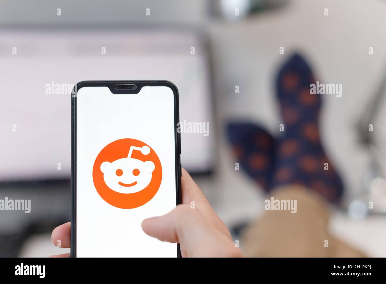 Minsk, Weißrussland - 31, Januar, 2021: Reddit-Logo auf dem Smartphone-Bildschirm in männlichen Händen mit seinen Füßen auf dem Tisch Stockfoto