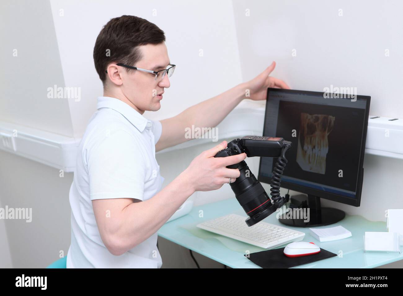 Der Zahnarzt hält eine Kamera mit Ringblitz in der Kamera. Arztarbeitsplatz vor einem Computer. Bilder von Zähnen auf einem Computerbildschirm. Moderne Zahnmedizin. Volum Stockfoto