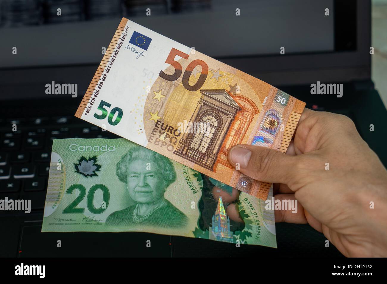 Eine Hand mit zwei Banknoten, eine von zwanzig kanadischen Dollar und die andere von fünfzig Euro Stockfoto