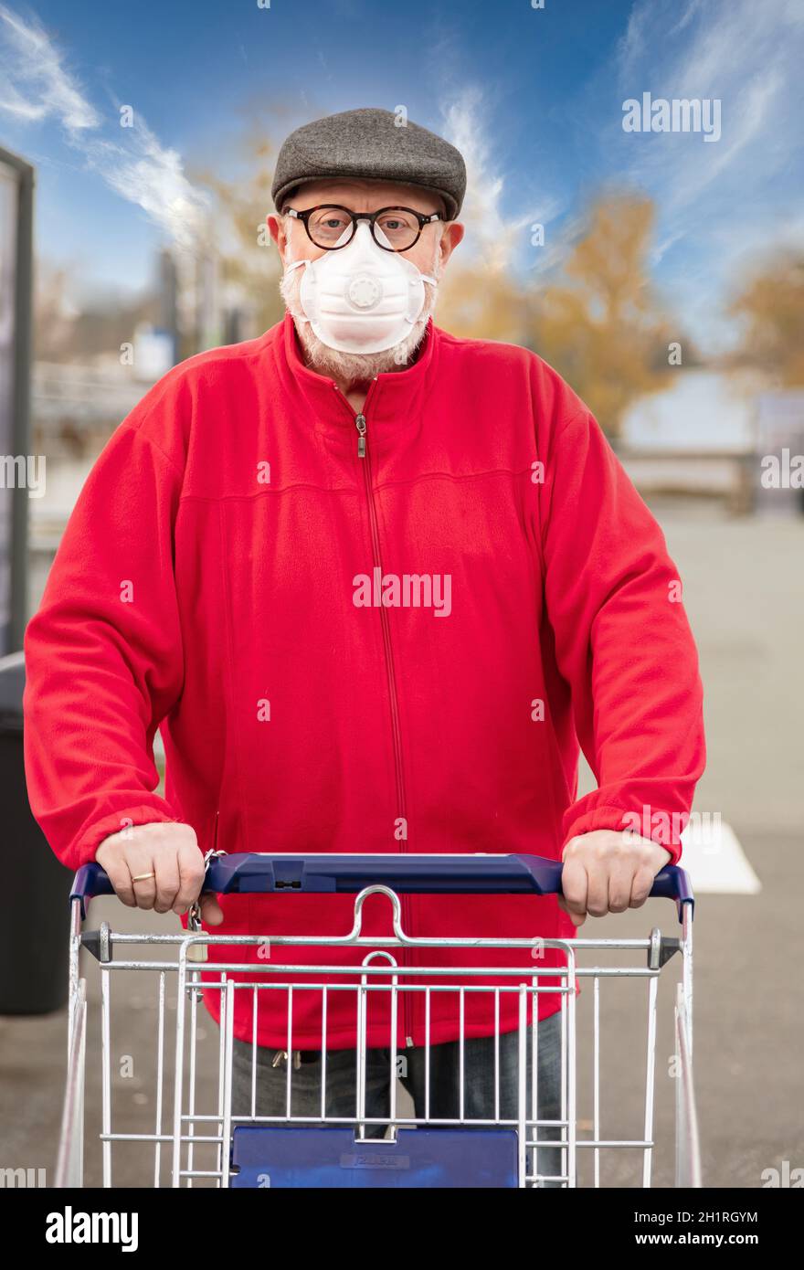 Ein älterer Mann trägt eine N95-Atemschutzmaske, während er einen Einkaufswagen außerhalb eines Lebensmittelladens schiebt. Der Mann schützt sich vor Coronavirus und Stockfoto