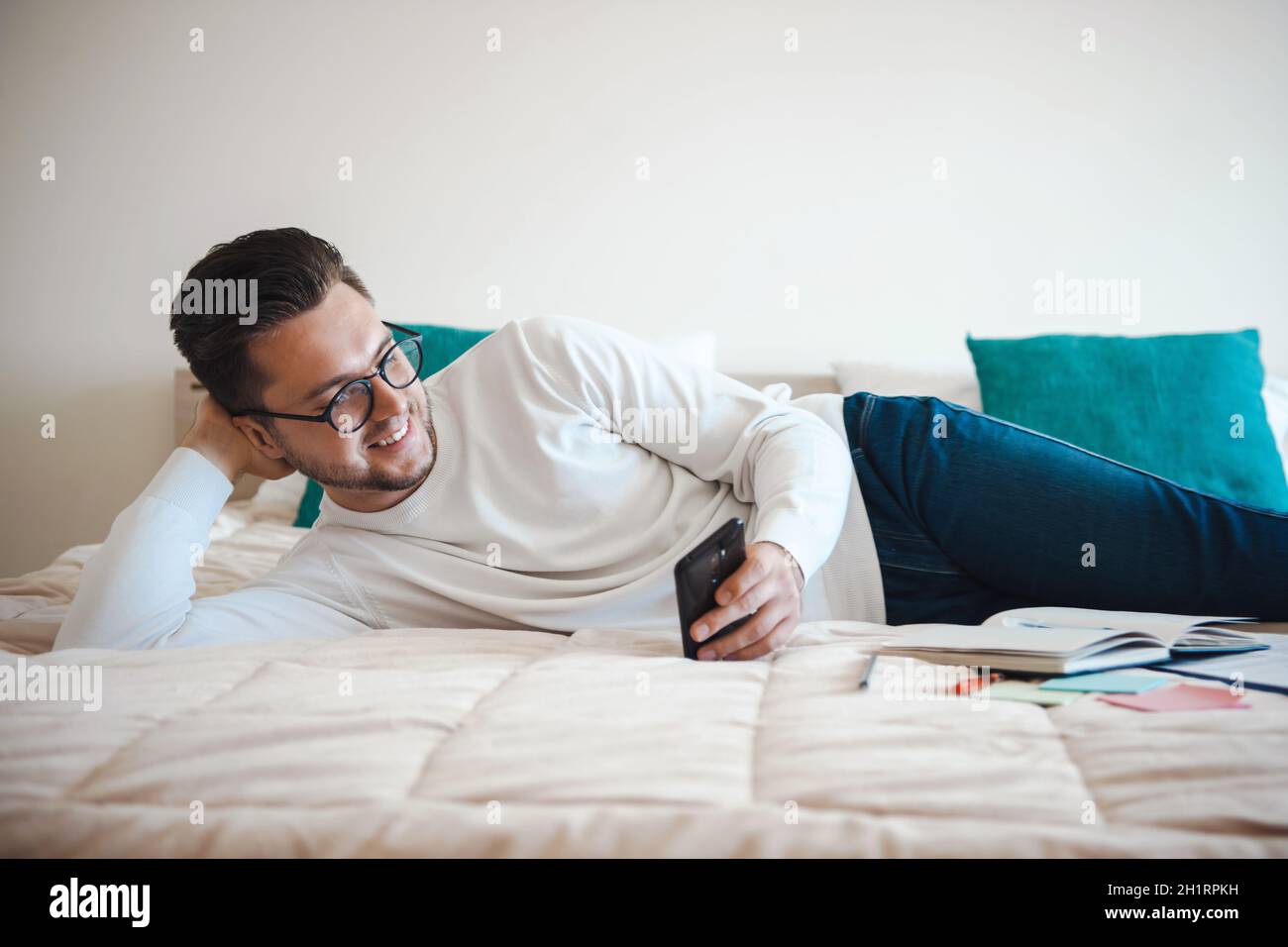Mann, der auf einer Seite auf dem Bett liegt, mit einer Hand unter dem Kopf und mit den anderen, die Botschaften schreiben Stockfoto