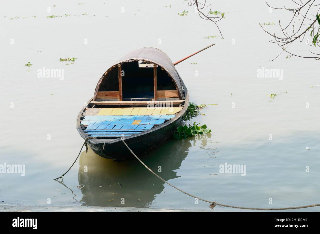 Ein Holzboot am Flussufer. Ein Fischerboot befestigt sich am wunderschönen Flussufer am tropischen Strand bei Sonnenuntergang. Sonnenlicht Reflexionen auf fließendem Wasser. Kerala Stockfoto