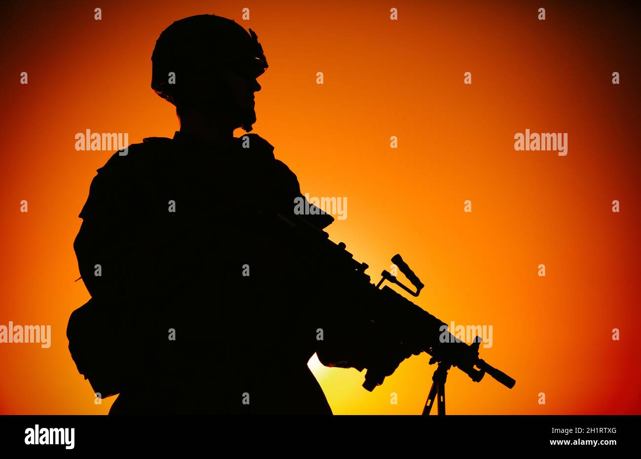 Silhouette der Armee Infanterie Soldat, Kommando im Kampfhelm, bewaffnete leichte Maschinengewehr, auf dem Hintergrund des Ozeans Horizont und Sonnenuntergang stehen. Marine Co Stockfoto