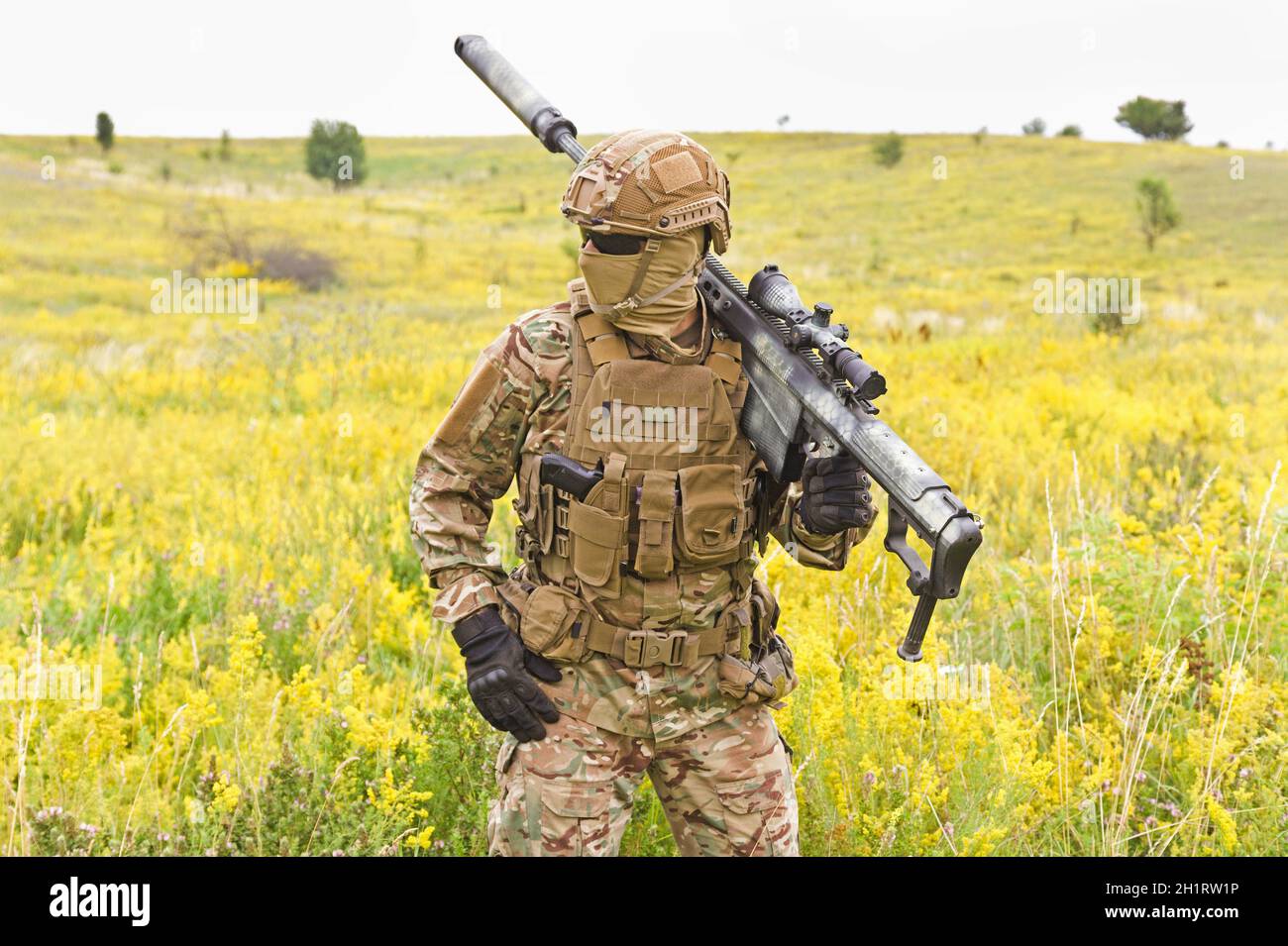 Soldat in einer speziellen Militäruniform, mit einem Helm auf dem Kopf und mit einem Scharfschützengewehr auf dem Feld Stockfoto