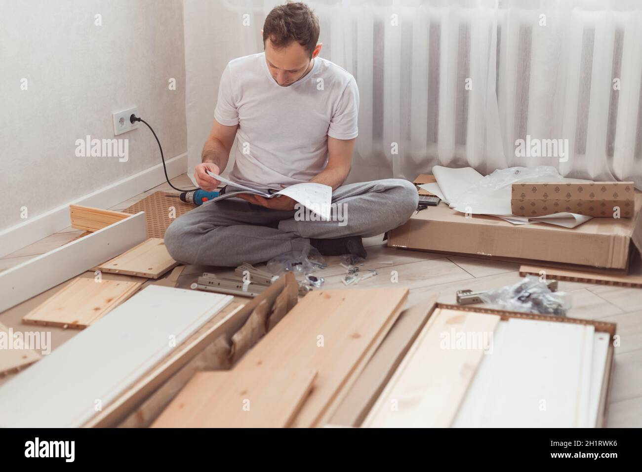 Verwirrter Mann, der Holzmöbel zusammengebaut hat. Schwierigkeiten und Nachteile der Selbstmontage der Möbel zu Hause ohne Meister. Mann liest instructi Stockfoto