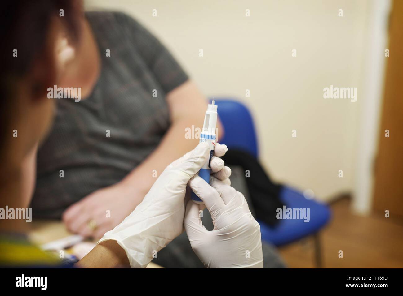 Weibliche GP-Chirurgie Krankenschwester trägt Handschuhe macht sich bereit, eine Injektion an eine weibliche Patientin in einer NHS-Chirurgie zu verabreichen Stockfoto