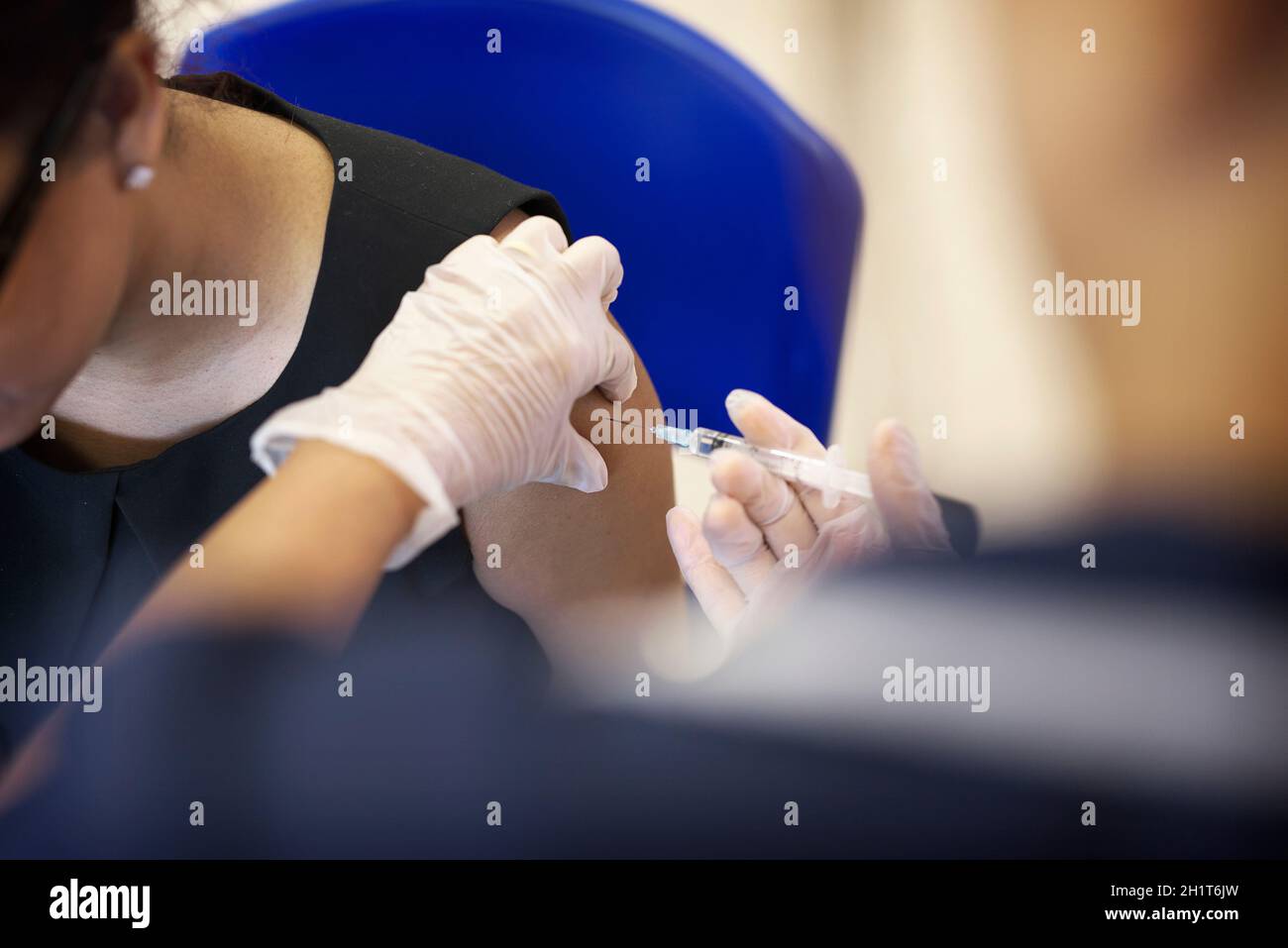 Weibliche, ältere Krankenschwester mit gemischter Rasse, verabreicht eine Grippeimpfung in den Arm einer weißen britischen Frau Stockfoto
