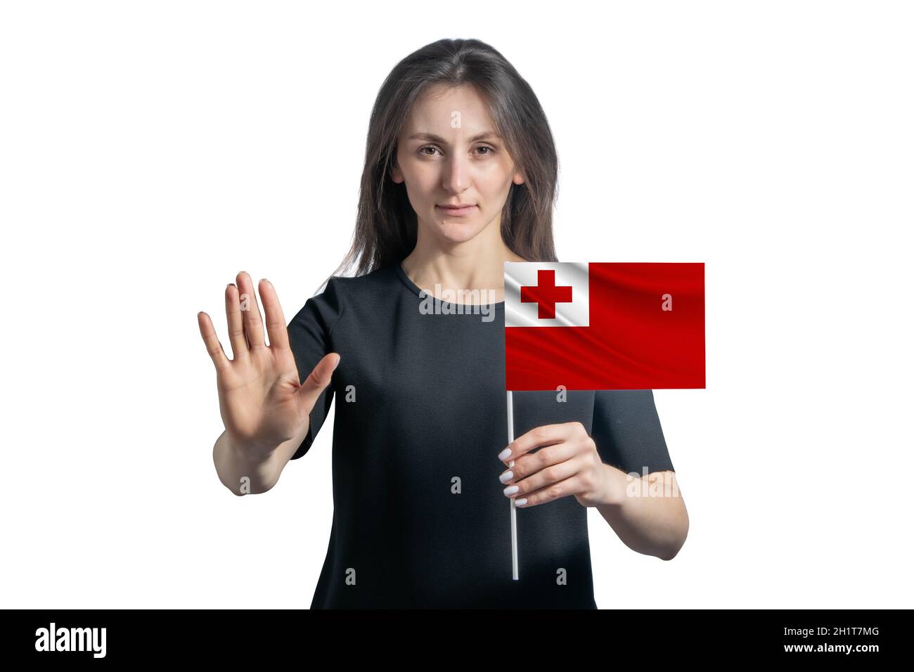Glückliche junge weiße Frau, die die Flagge von Tonga hält und mit einem ernsten Gesicht ein Hand-Stopp-Schild auf weißem Hintergrund zeigt. Stockfoto