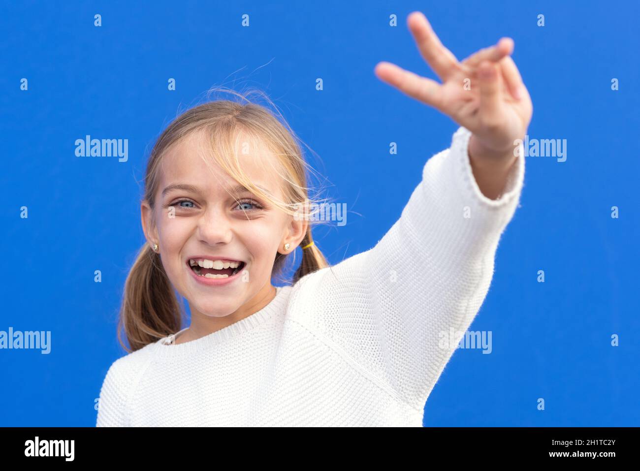 Junge schöne blonde Mädchen trägt lässige Pullover über blauen Hintergrund lächelnd Blick auf die Kamera zeigt Finger tun Siegeszeichen. Nummer zwei. H Stockfoto